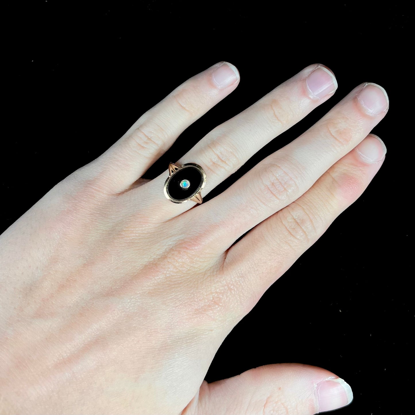 A yellow gold onyx ring set with a round cabochon cut opal bezel set into the onyx.