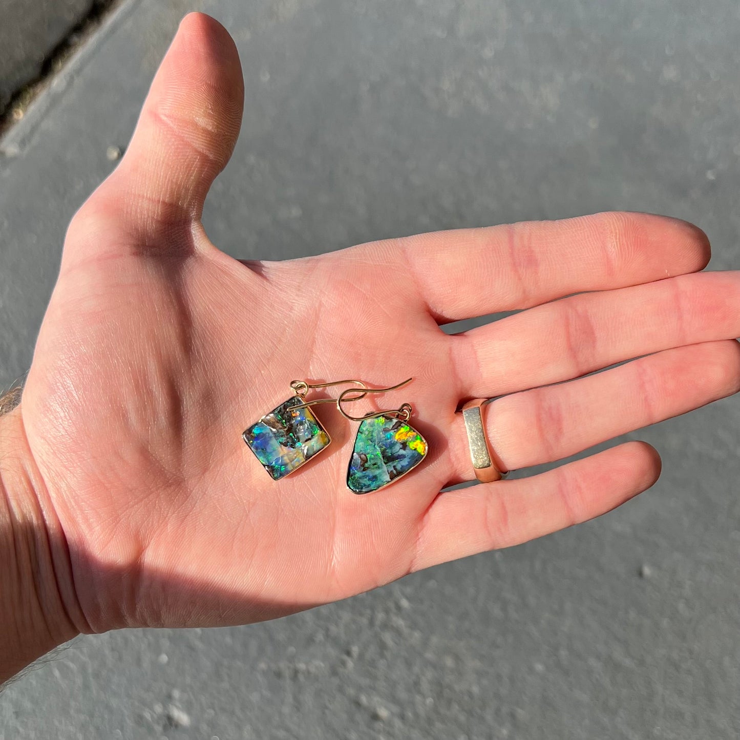 An asymmetric pair of French wire dangle yellow gold boulder opal earrings. One opal is a square, and the other is a triangle.
