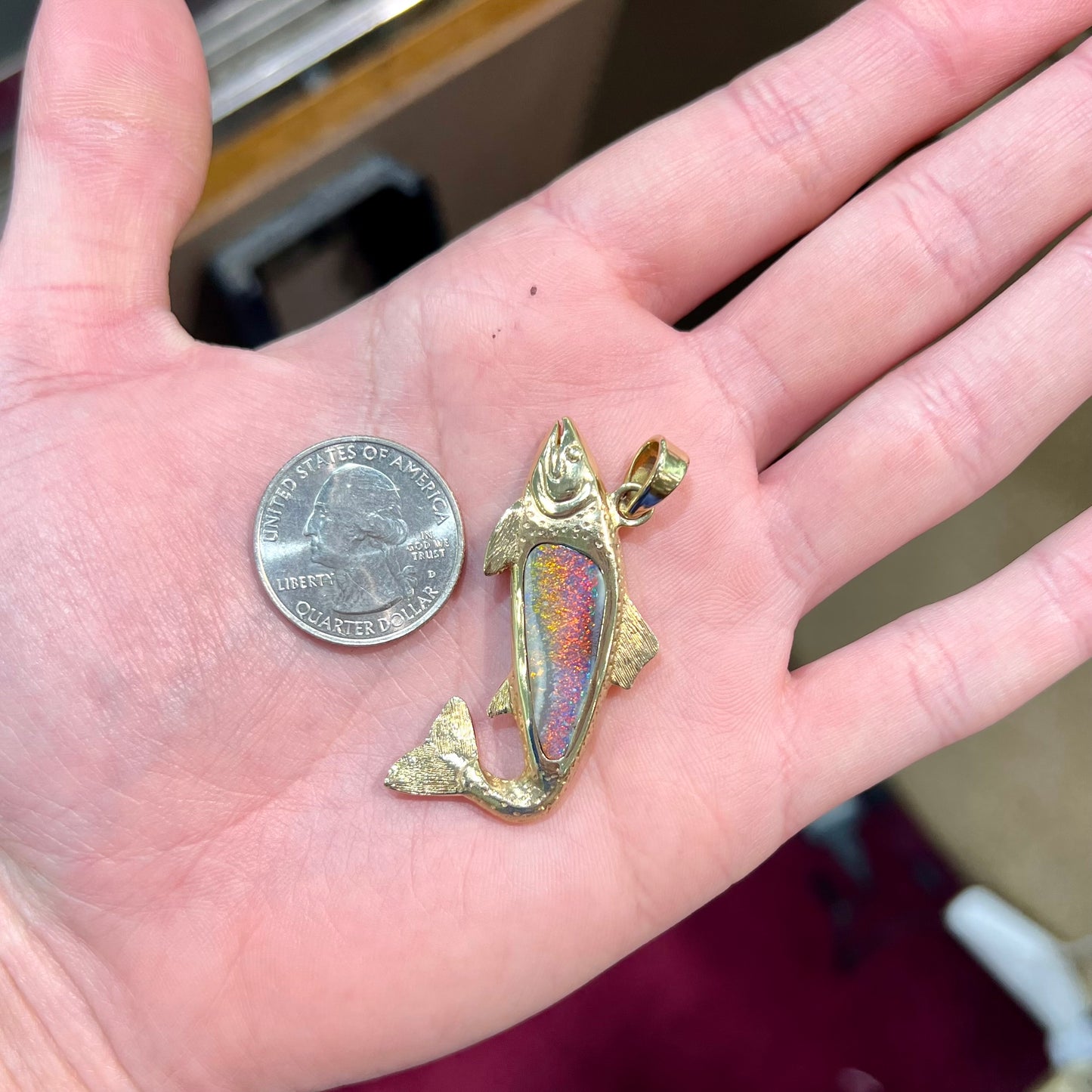 A yellow gold fish pendant detailed to look like a rainbow trout. The body of the fish is set with a color changing black opal stone.