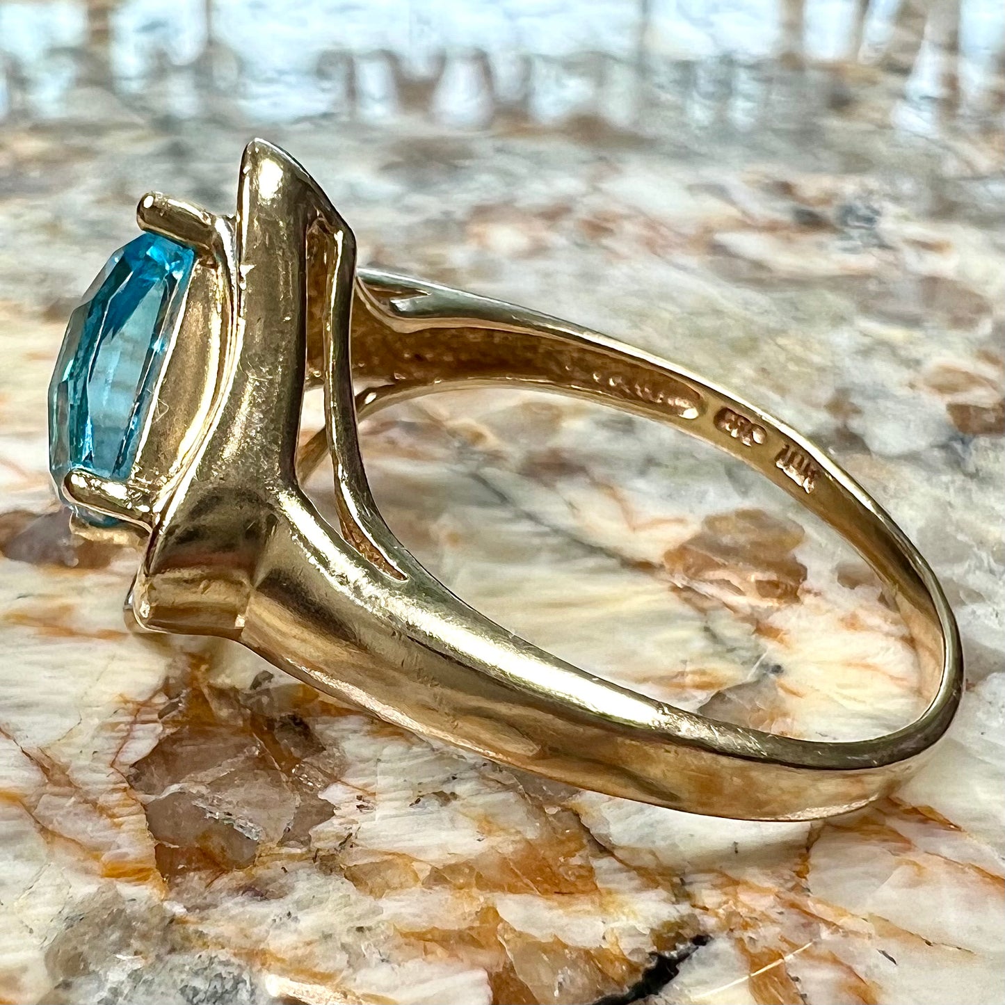 A checkerboard princess cut Swiss blue topaz ring. The stone is set in a yellow gold, diamond halo mounting.