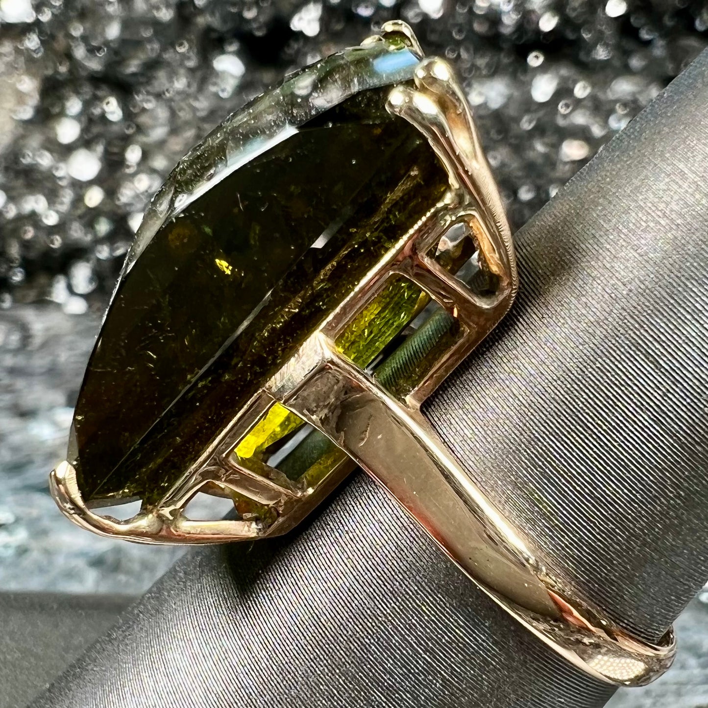 A faceted step-cut dark green tourmaline basket set solitaire ring cast in yellow gold.