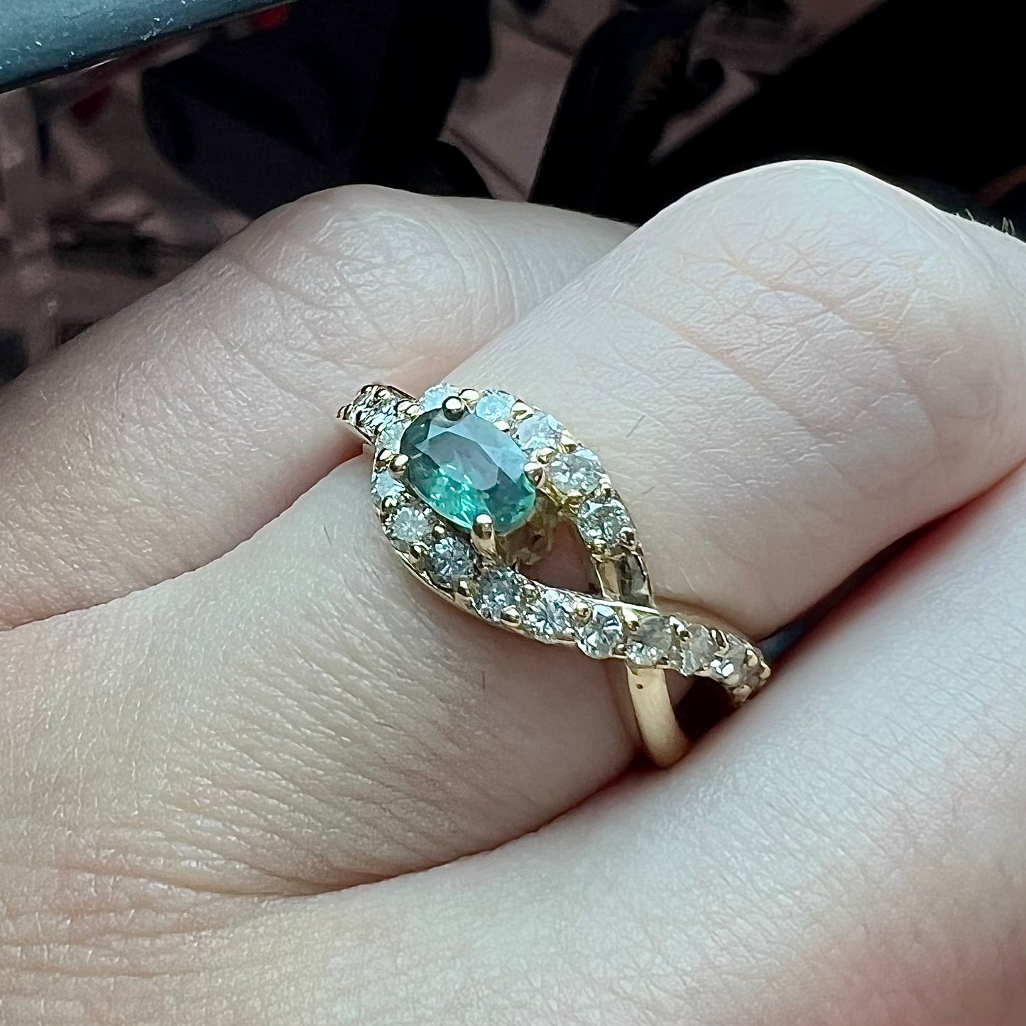 Yellow gold alexandrite and pave set diamond ladies' ring on a hand under white LED light.