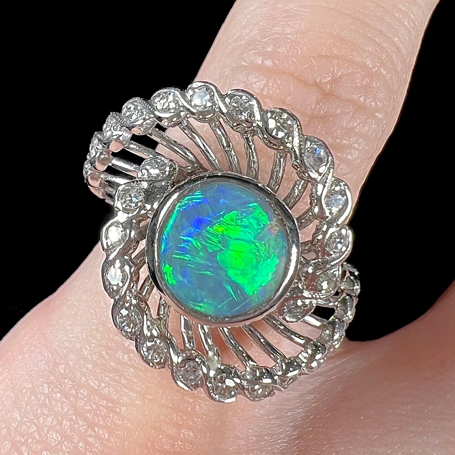 A white gold ring featuring a round cabochon cut black opal set in a swirl of round cut diamonds.