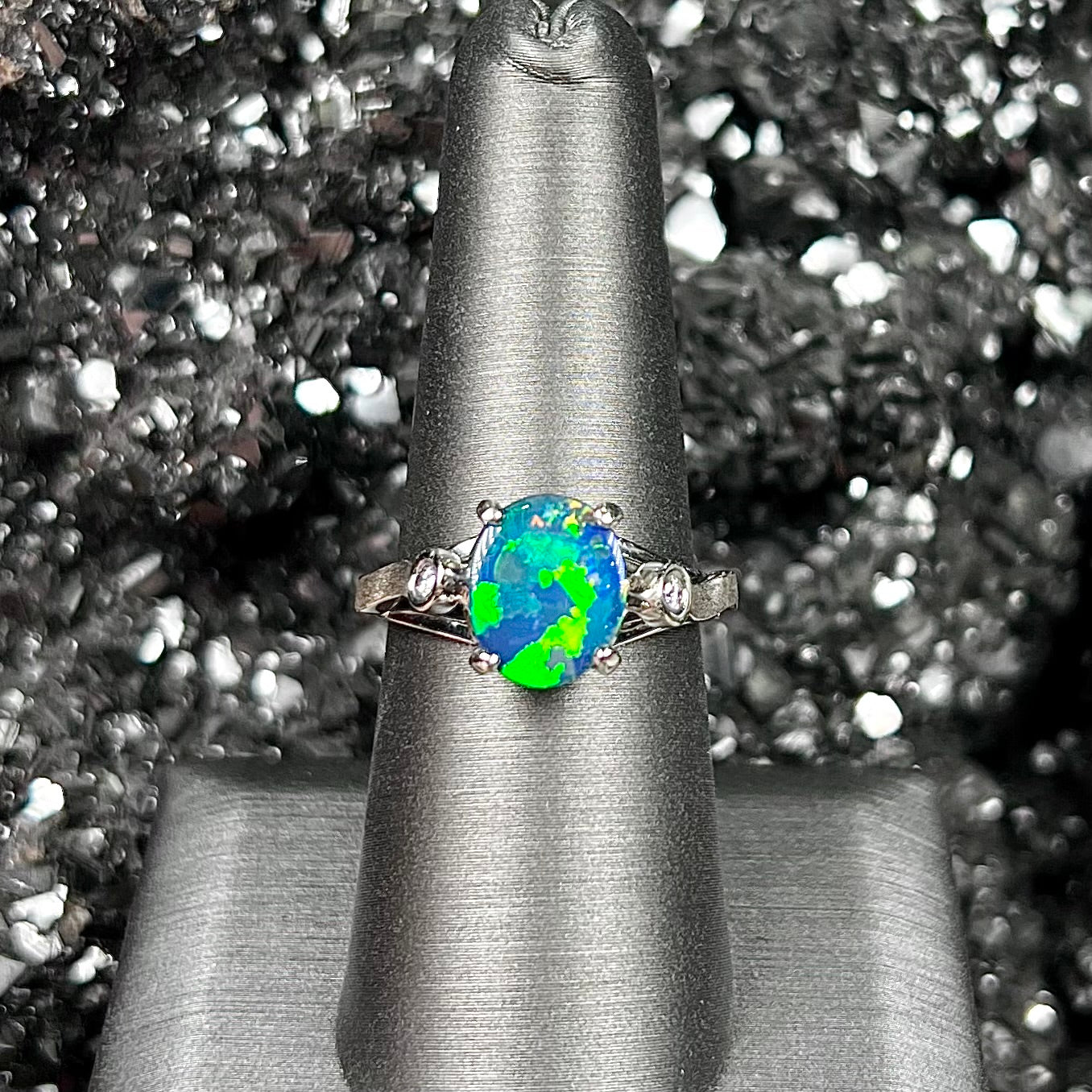 A white gold, oval cabochon cut black opal doublet ring set with two round diamond accent stones.