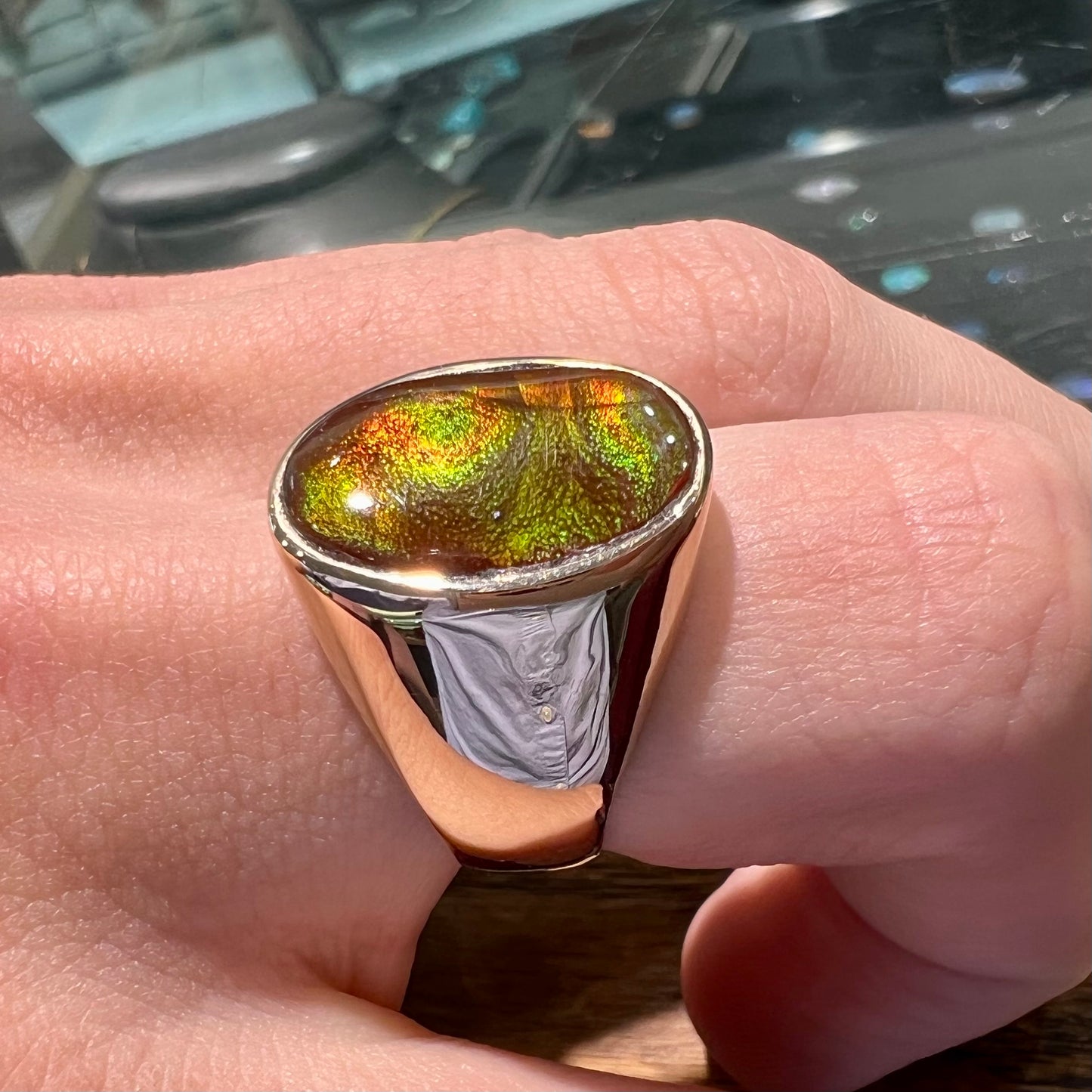 A yellow gold solitaire fire agate men's ring. The fire agate is oval shape, and red and green in color.
