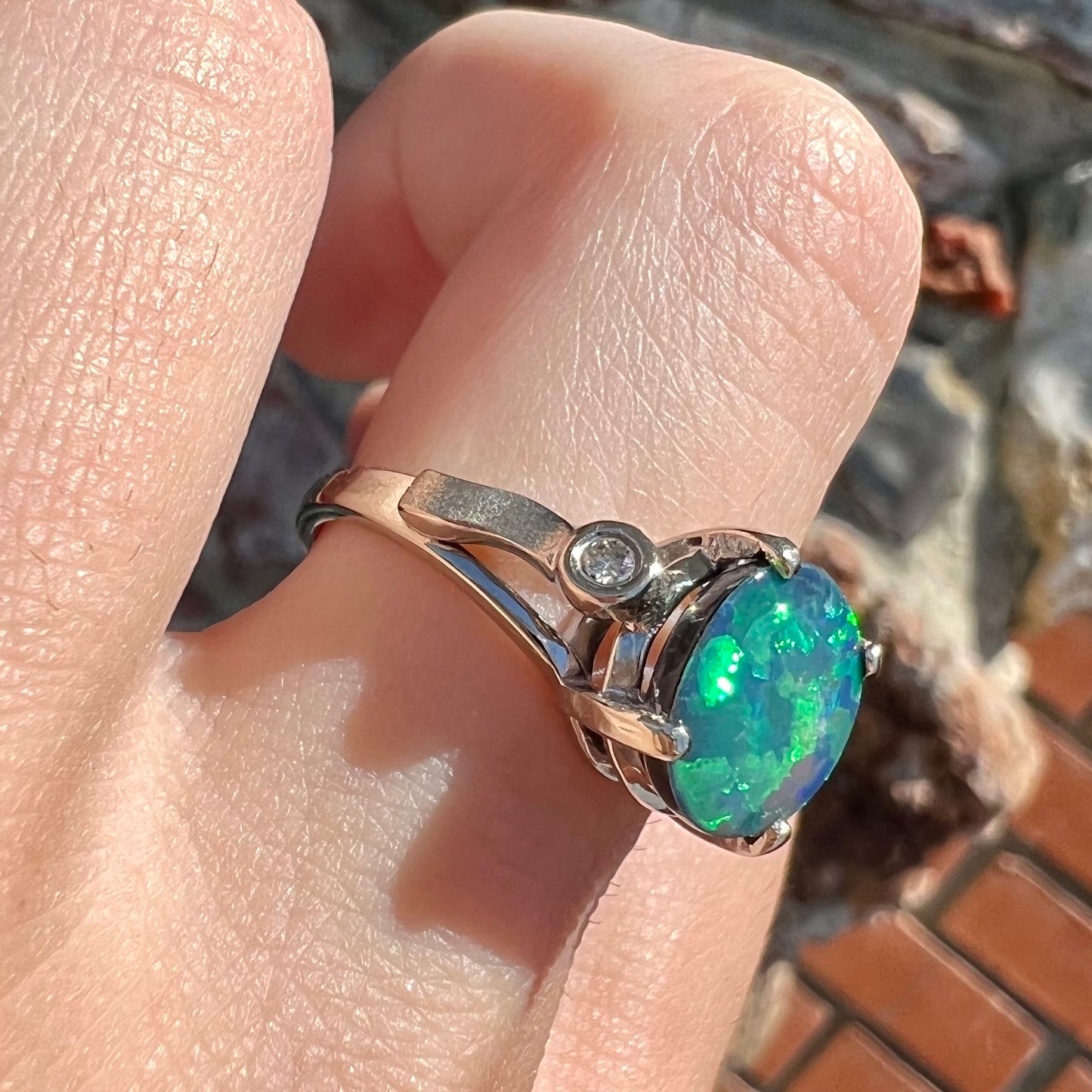 A white gold, oval cabochon cut black opal doublet ring set with two round diamond accent stones.