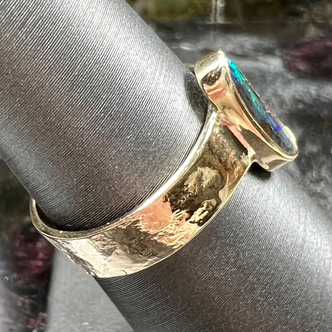 A blue green oval cabochon cut Australian boulder opal set in a yellow gold solitaire ring.