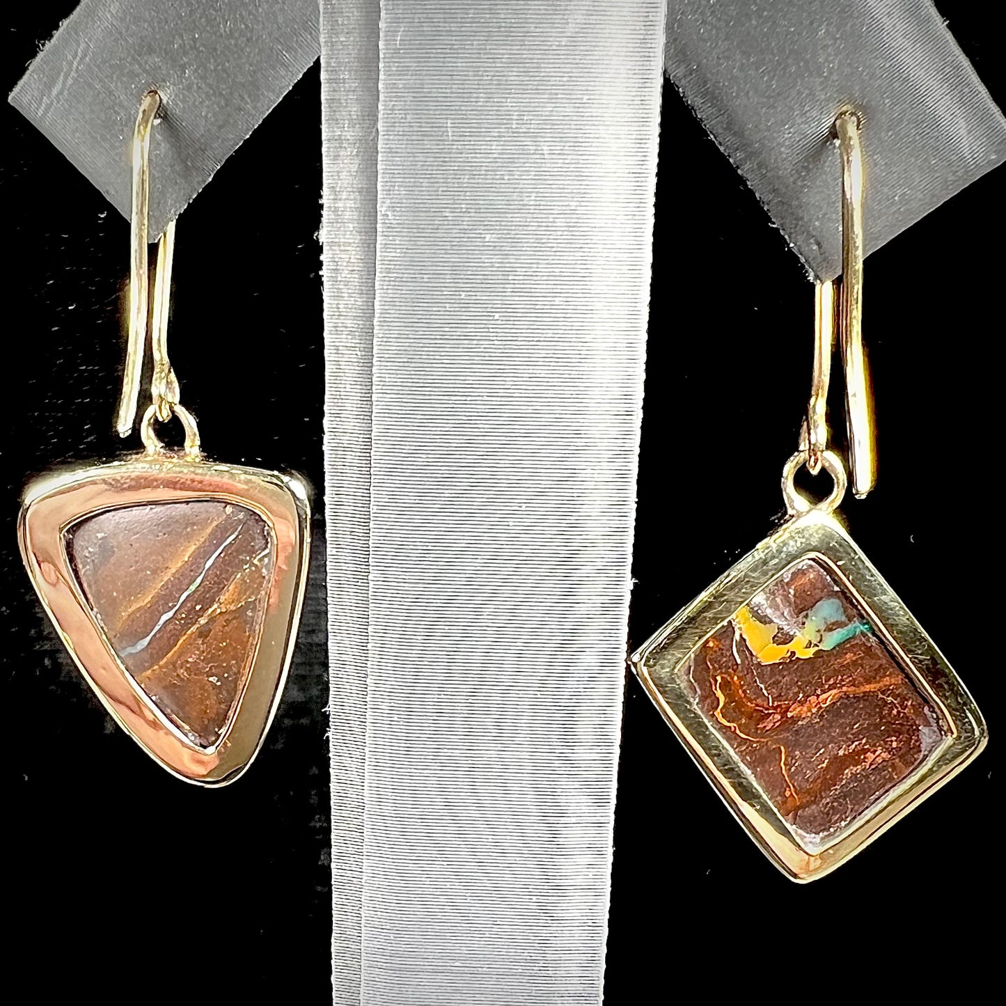 An asymmetric pair of French wire dangle yellow gold boulder opal earrings. One opal is a square, and the other is a triangle.