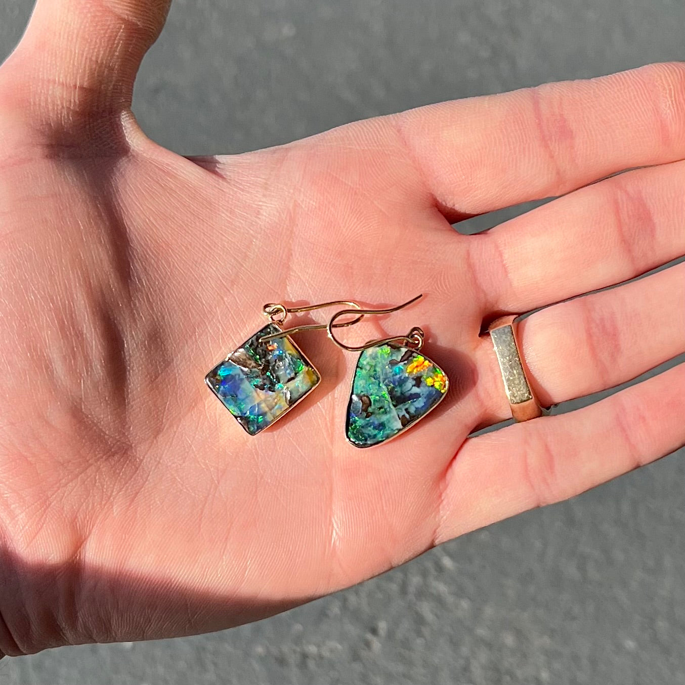 An asymmetric pair of French wire dangle yellow gold boulder opal earrings. One opal is a square, and the other is a triangle.