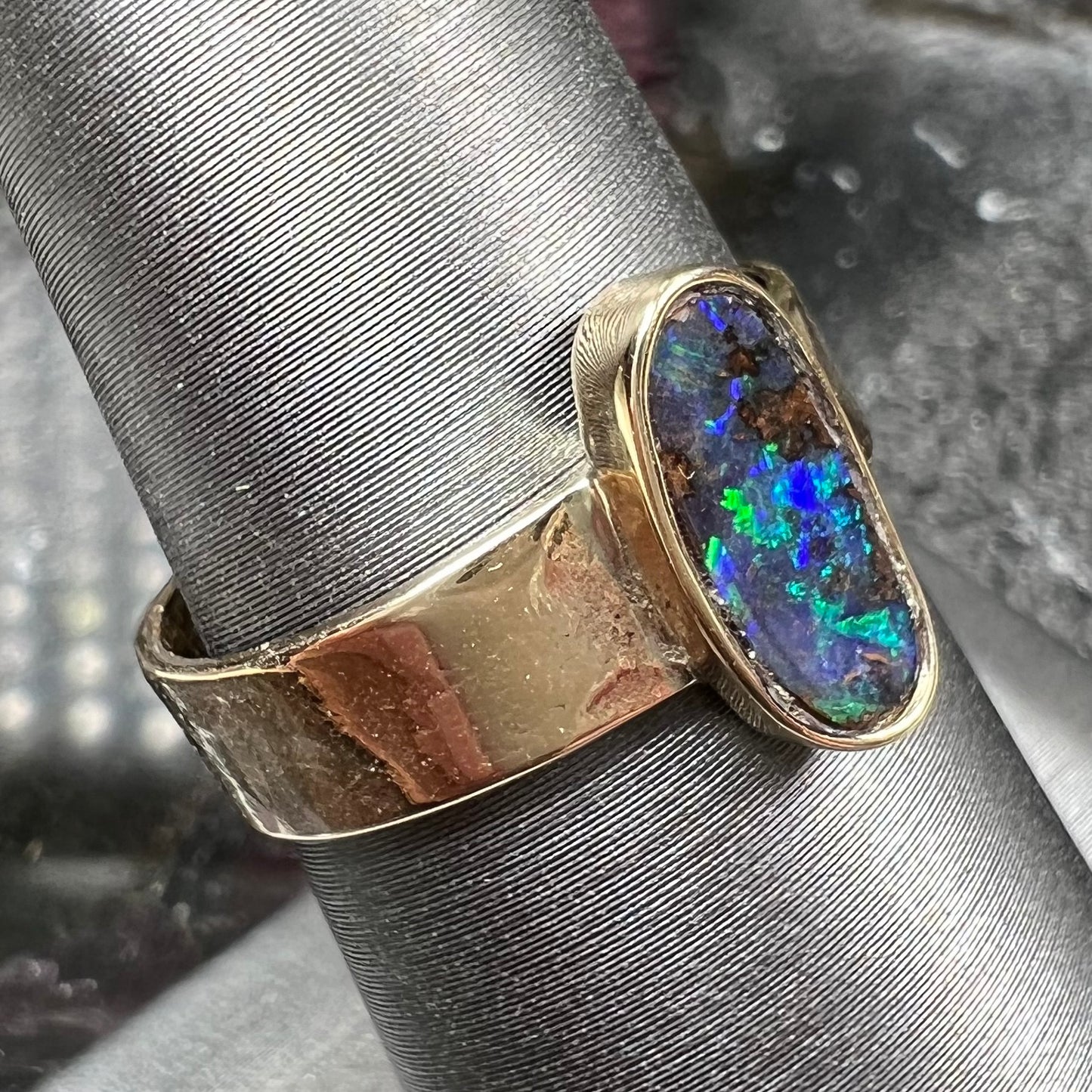 A blue green oval cabochon cut Australian boulder opal set in a yellow gold solitaire ring.