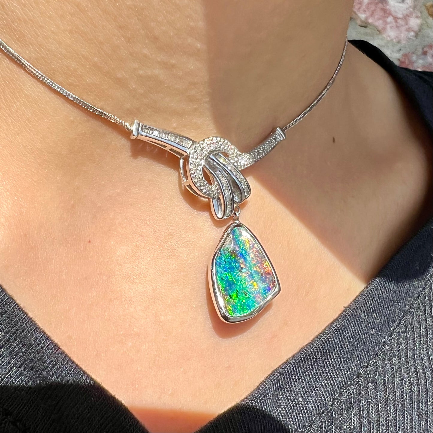 A white gold necklace set with diamonds and a dangling, bezel set boulder opal.