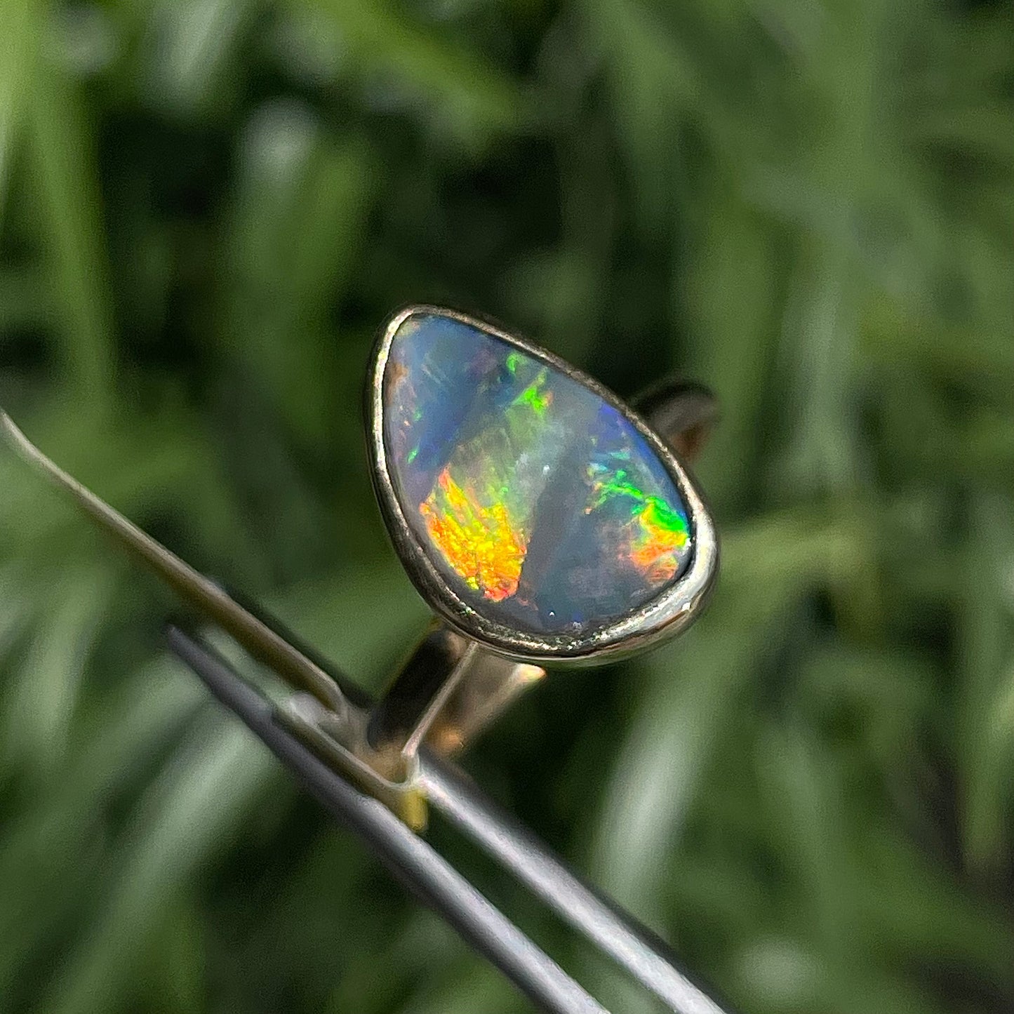 A freeform cut semi-black opal from Lightning Ridge, Australia set in a bezel set yellow gold solitaire ring.