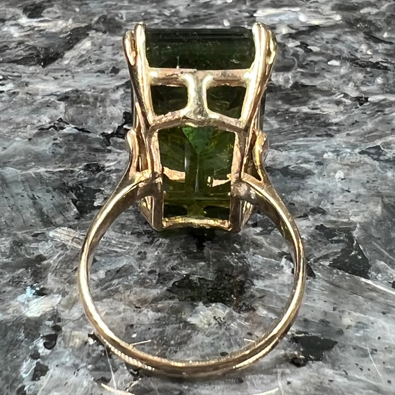 A faceted step-cut dark green tourmaline basket set solitaire ring cast in yellow gold.