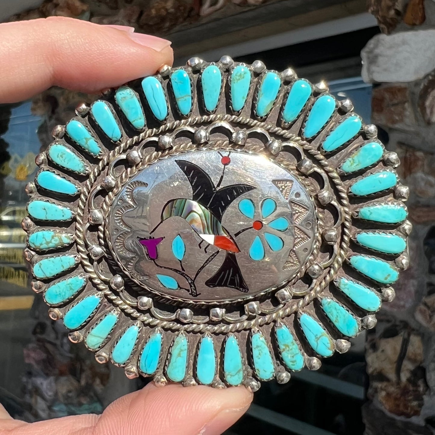 A unisex sterling silver belt buckle featuring the motif of a stone inlaid hummingbird set with petit point turquoise accents, handmade by Navajo artist, Leo G. Harvey.