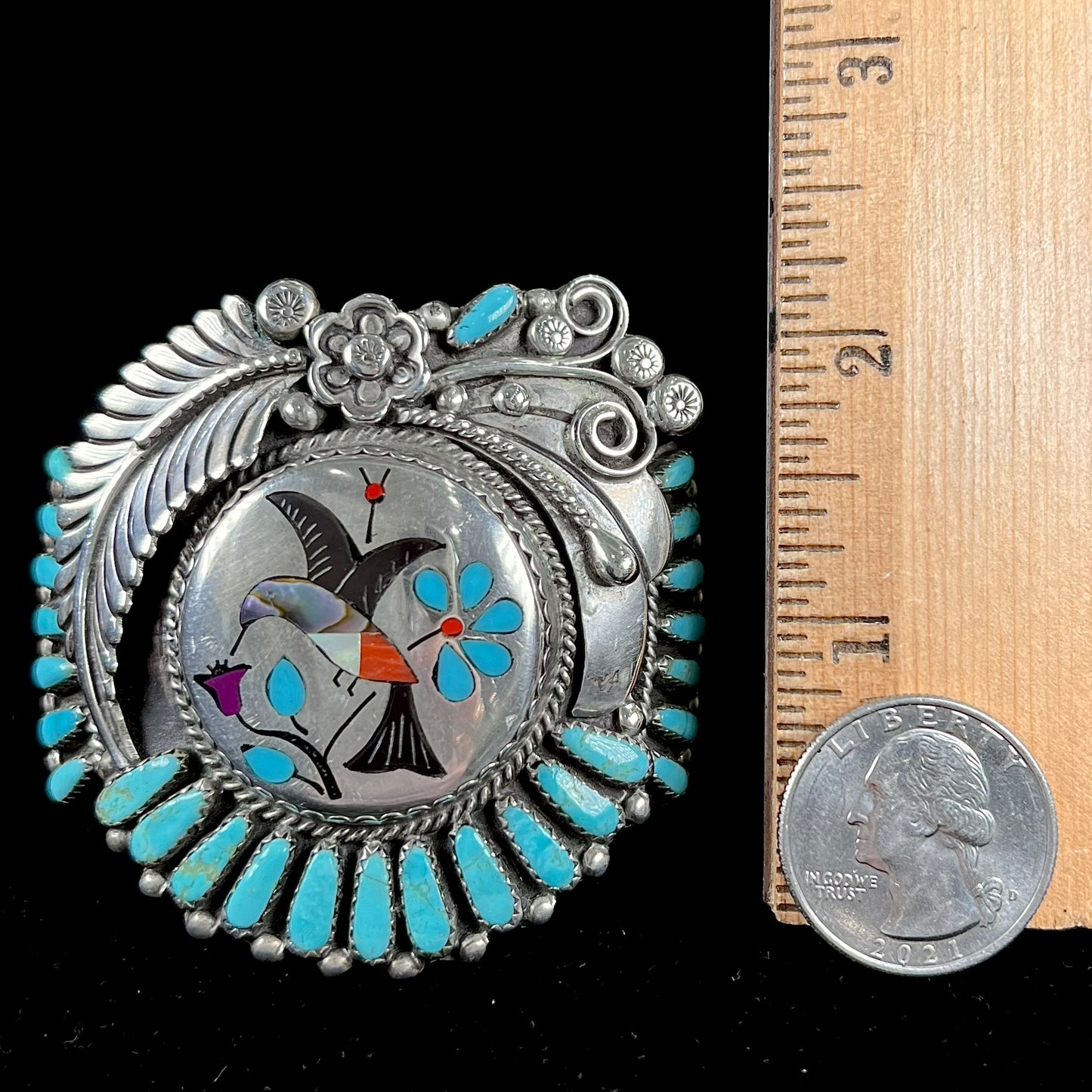 A sterling silver cuff bracelet featuring the motif of a stone inlaid hummingbird with petit point turquoise accents, handmade by Navajo artist Leo G. Harvey.