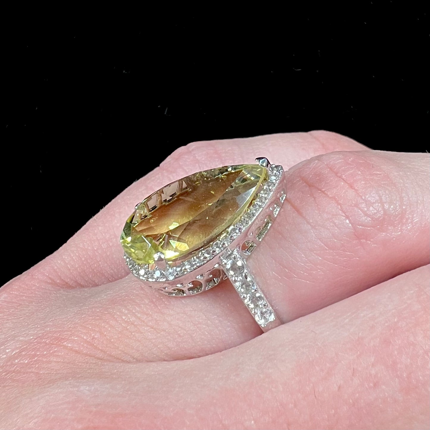 A pear shape lemon quartz set in a sterling silver and white topaz halo ring.