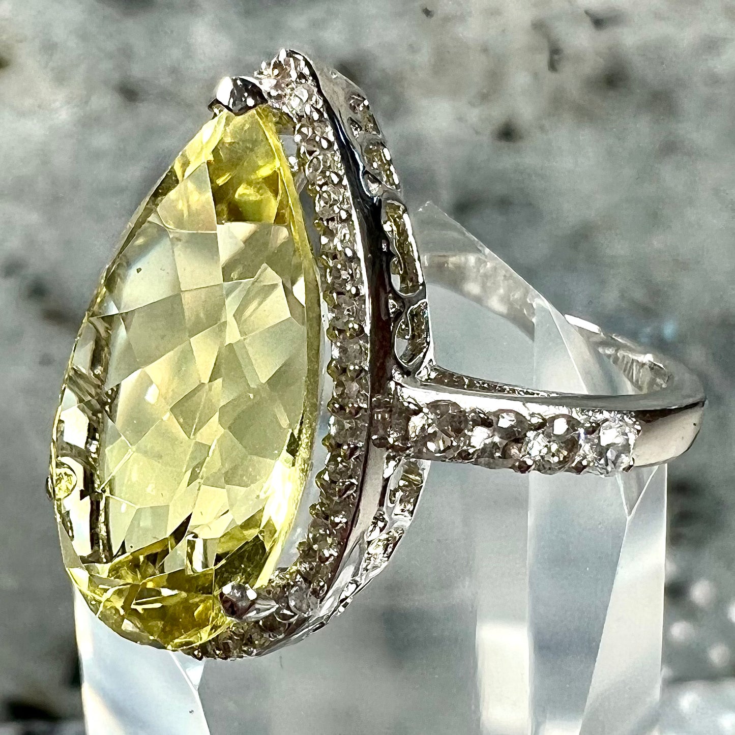 A pear shape lemon quartz set in a sterling silver and white topaz halo ring.
