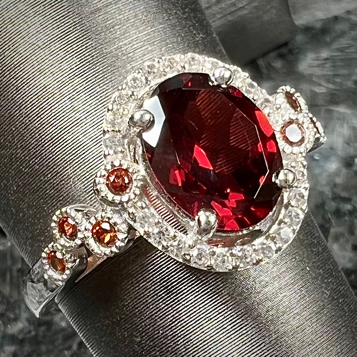 A silver garnet and CZ halo ring. The center stone is a red almandine garnet, and the side garnets are orange.