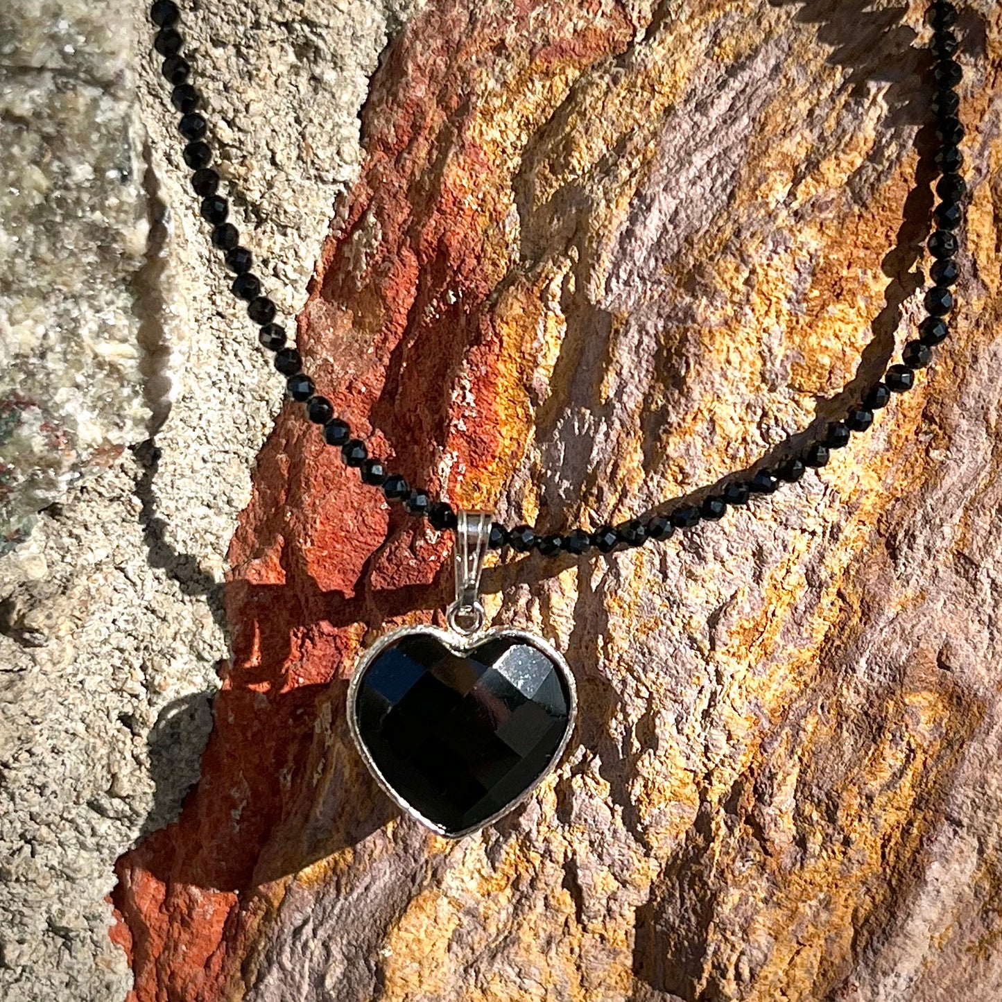 A silver heart shape black stone necklace. The heart is a faceted cut black spinel, and the pendant is on faceted black spinel beads.