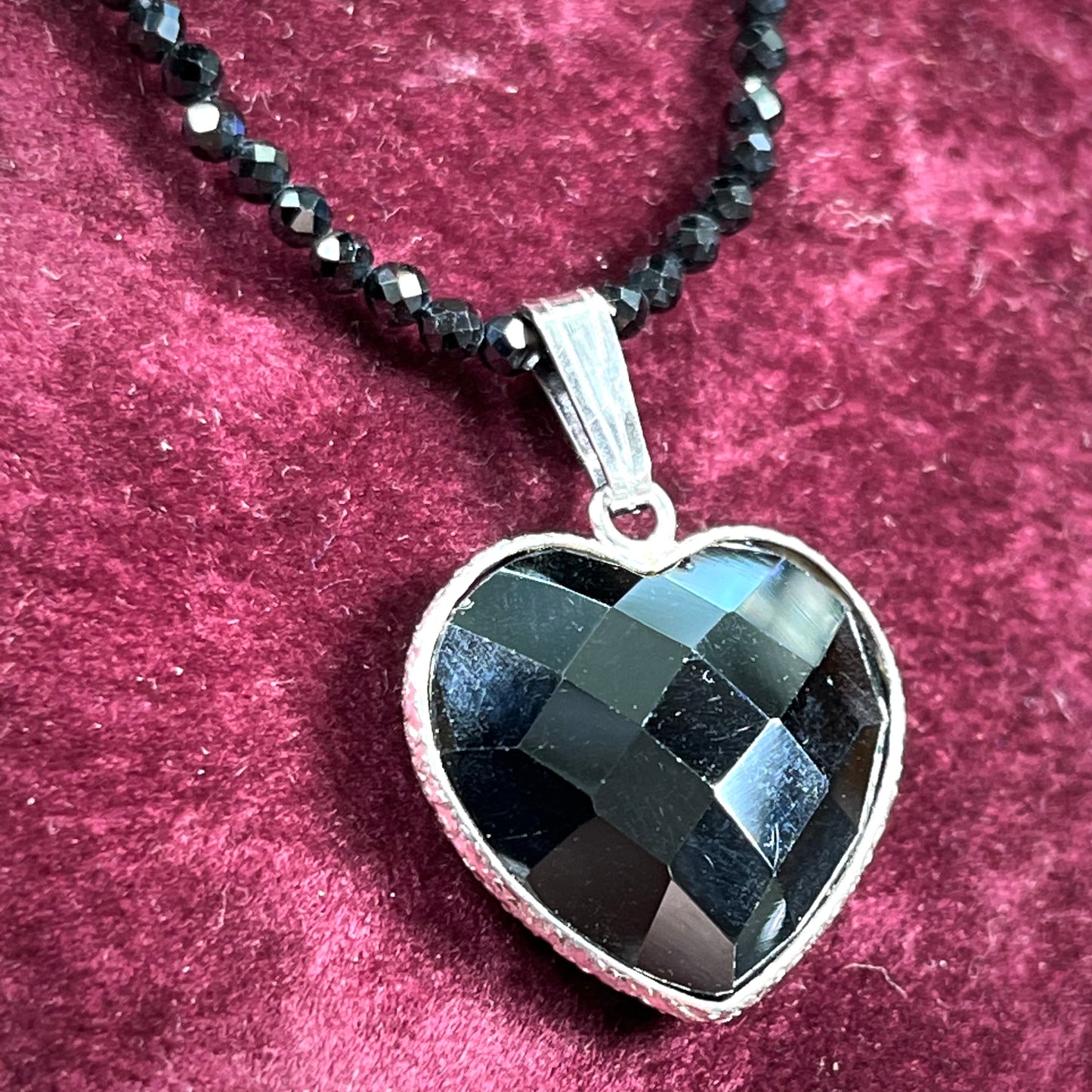 A silver heart shape black stone necklace. The heart is a faceted cut black spinel, and the pendant is on faceted black spinel beads.