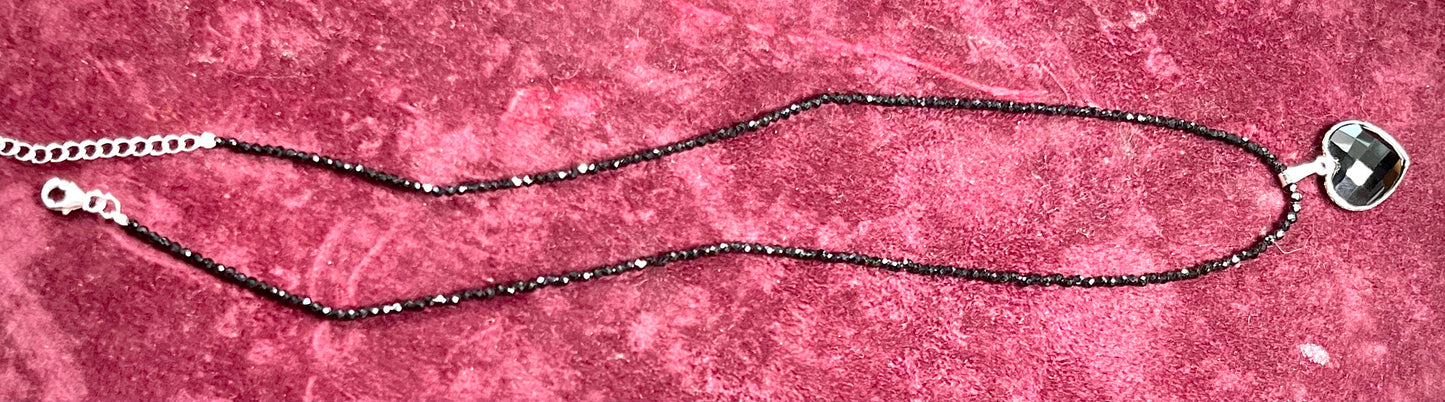 A silver heart shape black stone necklace. The heart is a faceted cut black spinel, and the pendant is on faceted black spinel beads.
