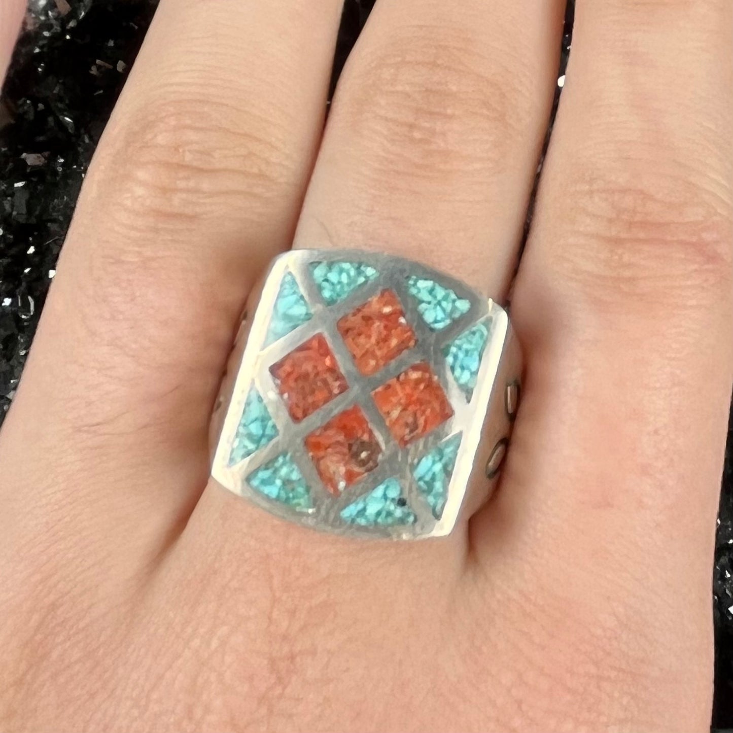 A men's sterling silver inlay ring set with sections of crushed blue turquoise and crushed red coral.