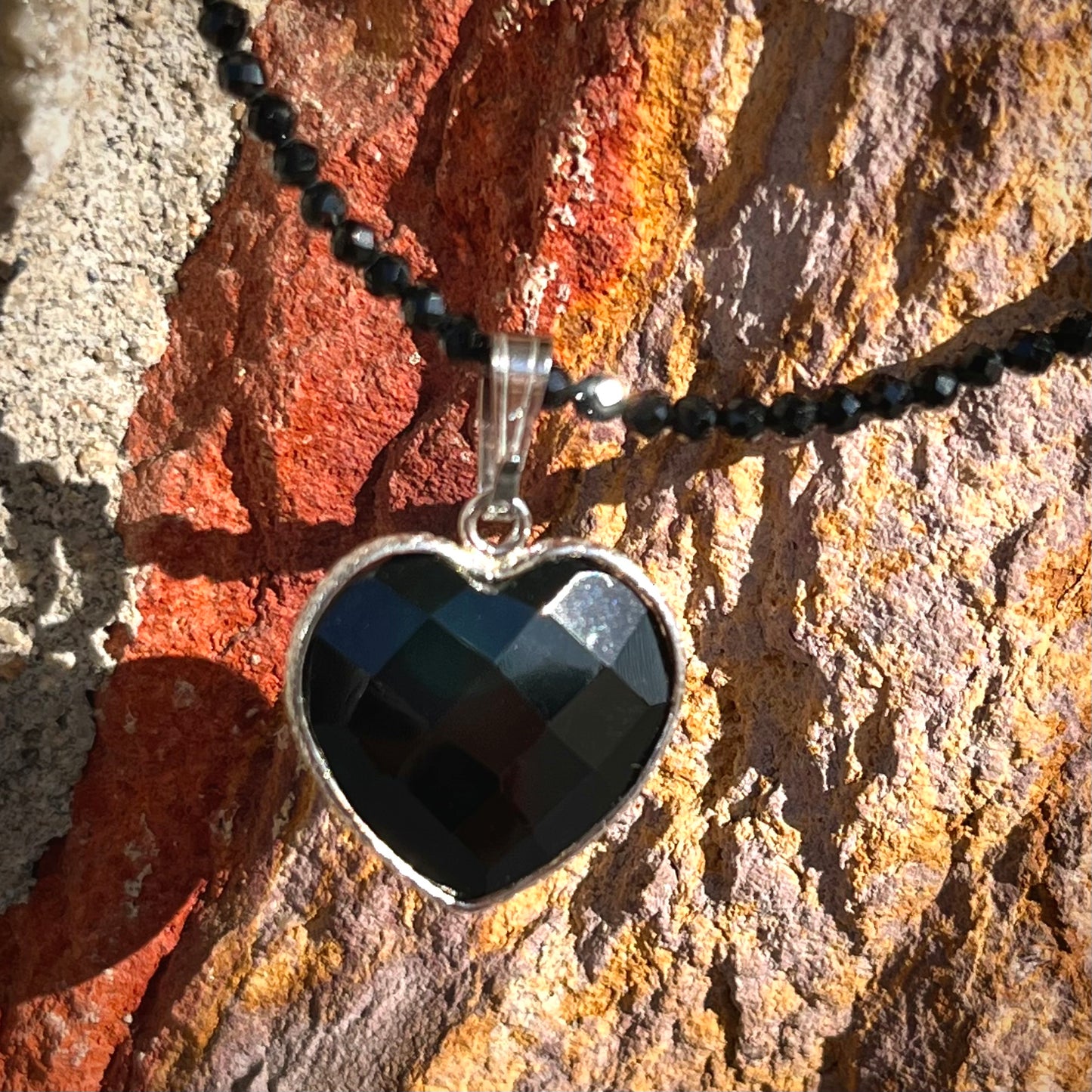 A silver heart shape black stone necklace. The heart is a faceted cut black spinel, and the pendant is on faceted black spinel beads.