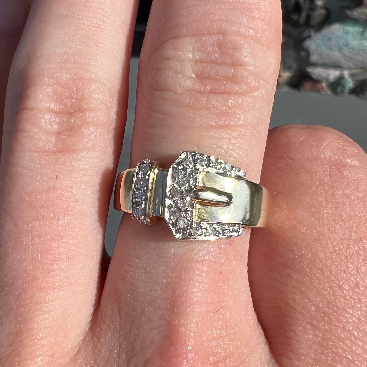 A yellow gold buckle ring set with round diamonds in the buckle.