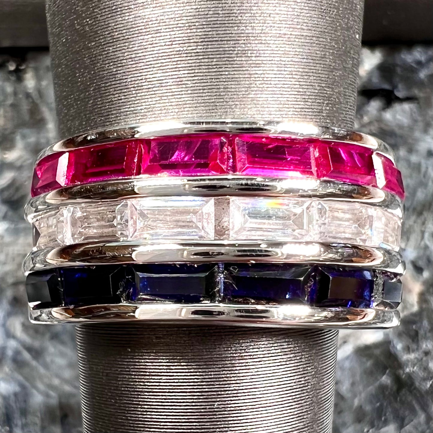 A silver ring set with red, white, and blue baguette cut stones. The gallery features two stars.