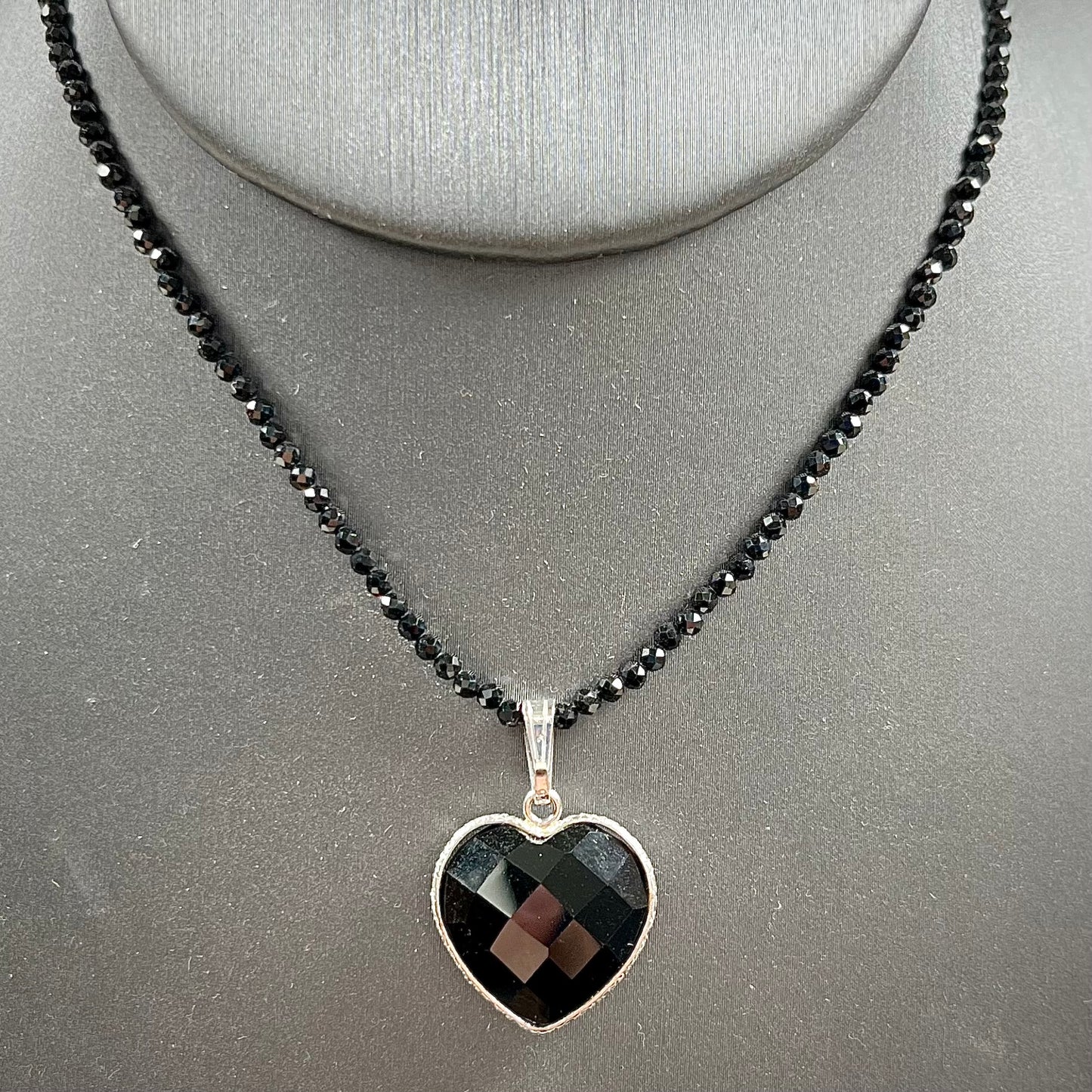 A silver heart shape black stone necklace. The heart is a faceted cut black spinel, and the pendant is on faceted black spinel beads.
