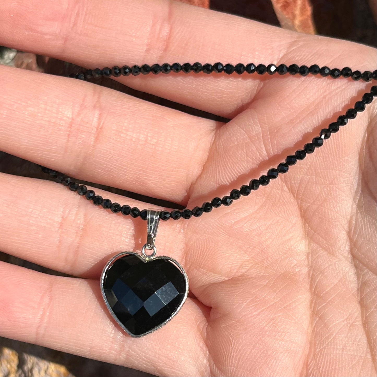 A silver heart shape black stone necklace. The heart is a faceted cut black spinel, and the pendant is on faceted black spinel beads.