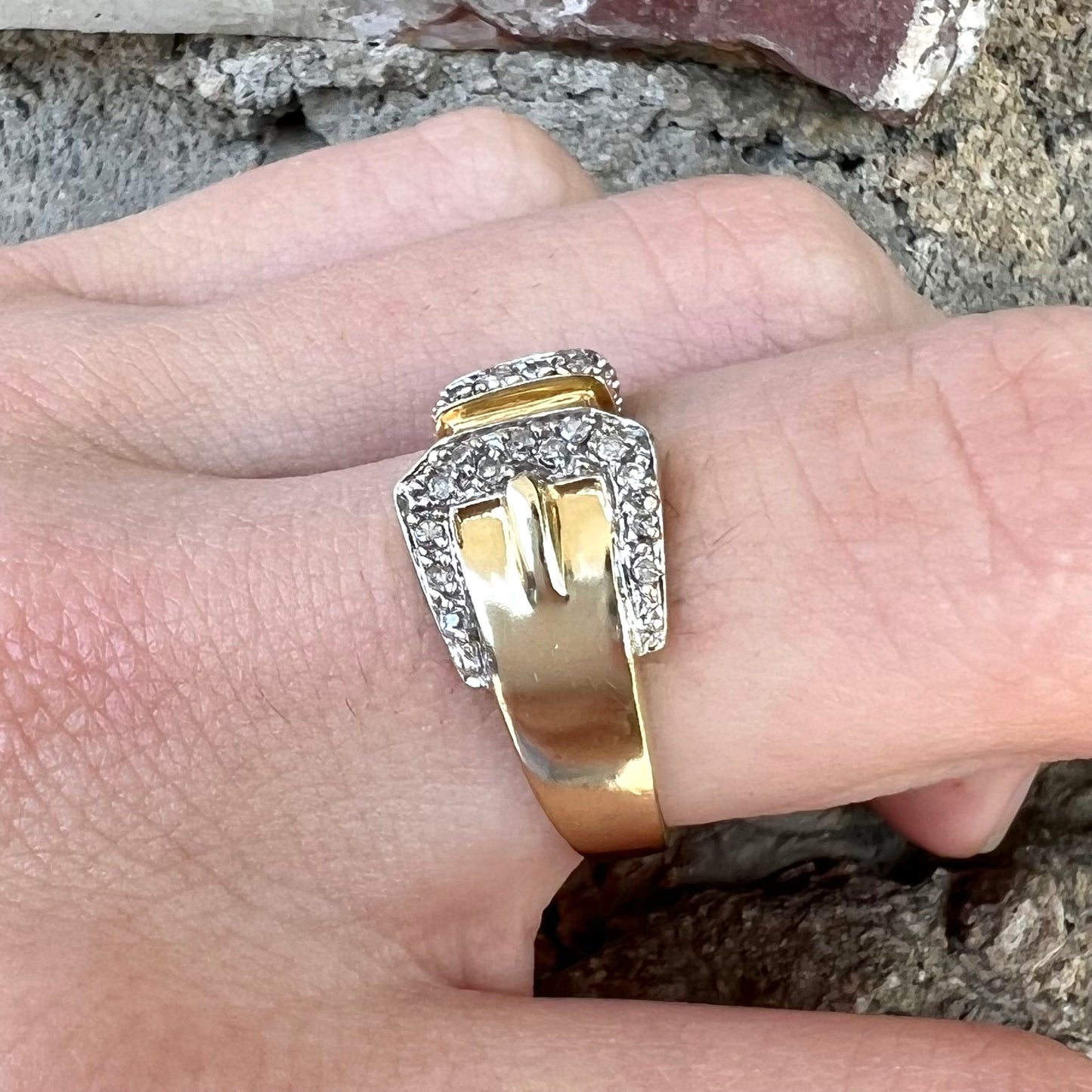 A yellow gold buckle ring set with round diamonds in the buckle.