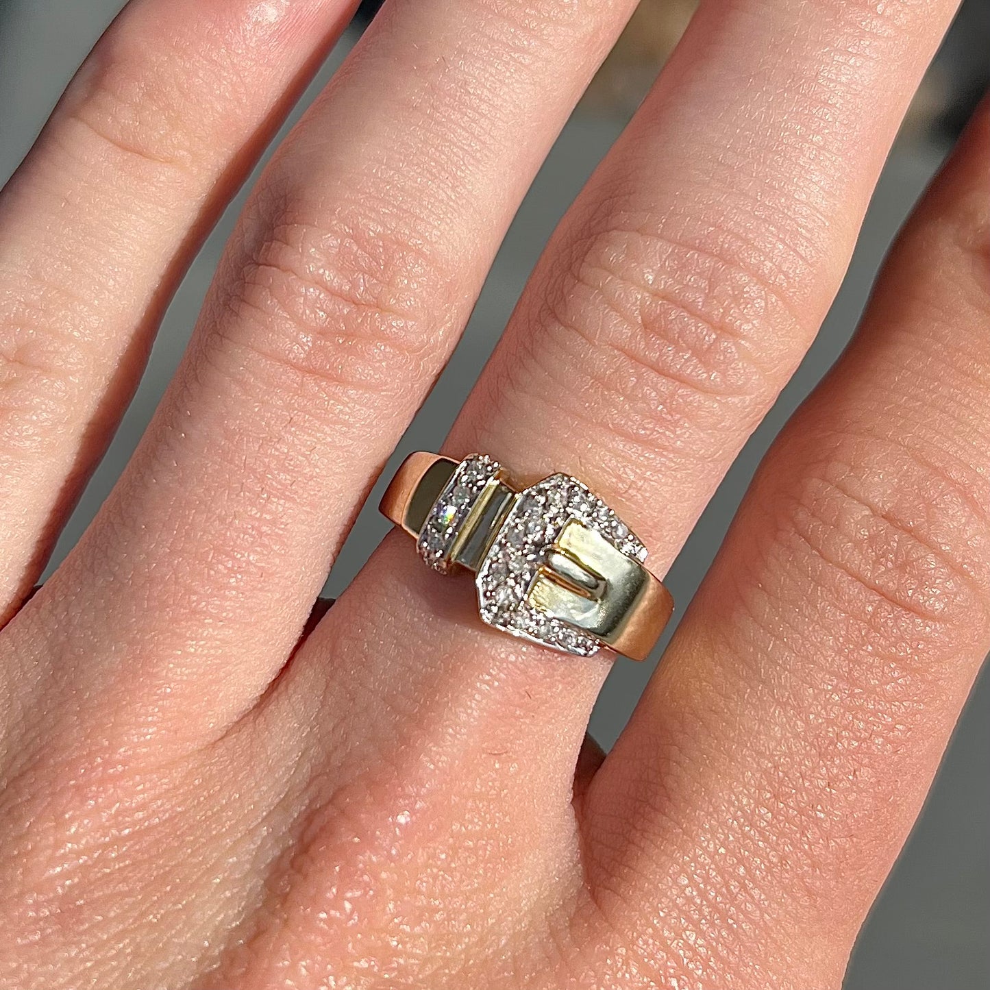 A yellow gold buckle ring set with round diamonds in the buckle.