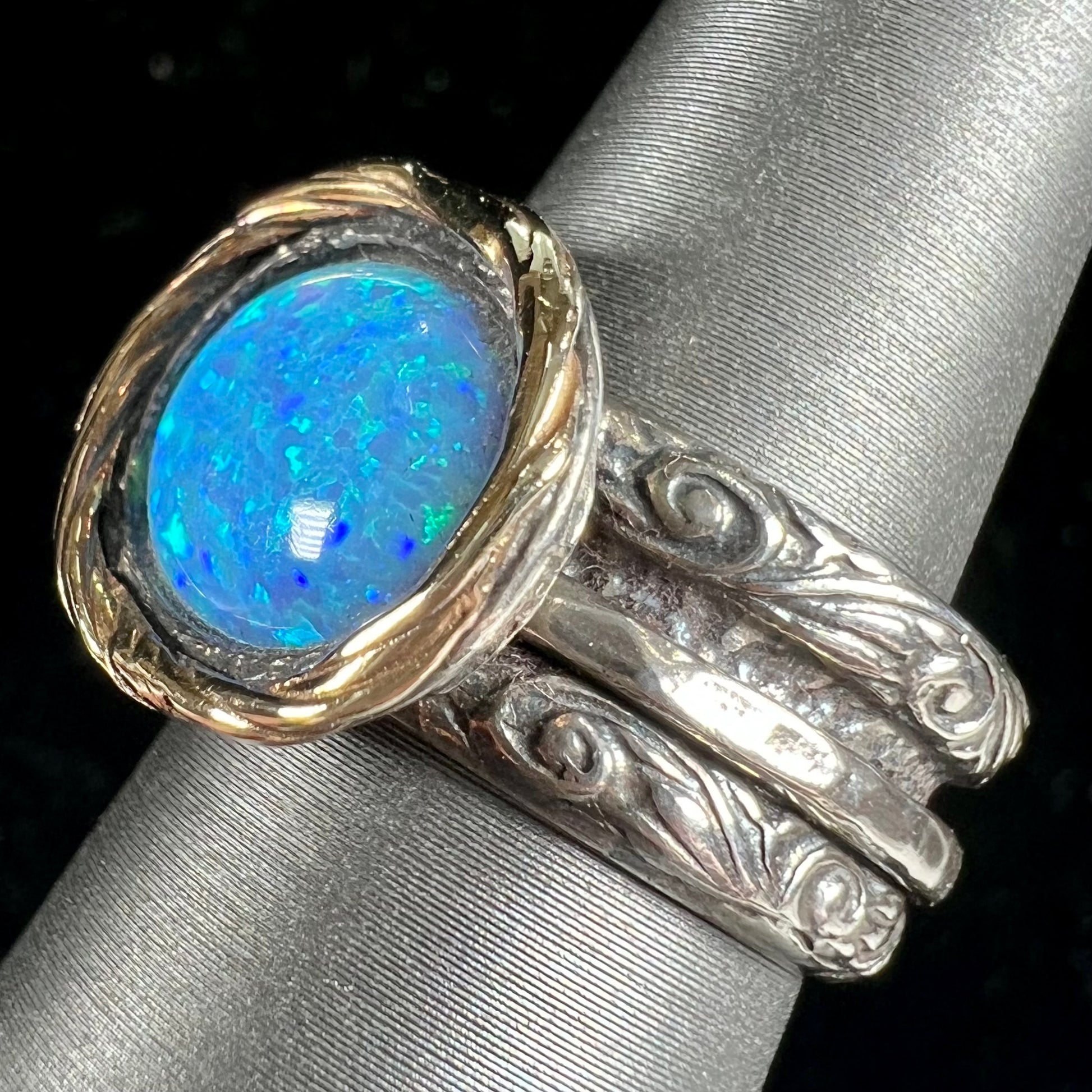 A filigree etched two tone silver and gold spinner ring set with a lab created black opal.