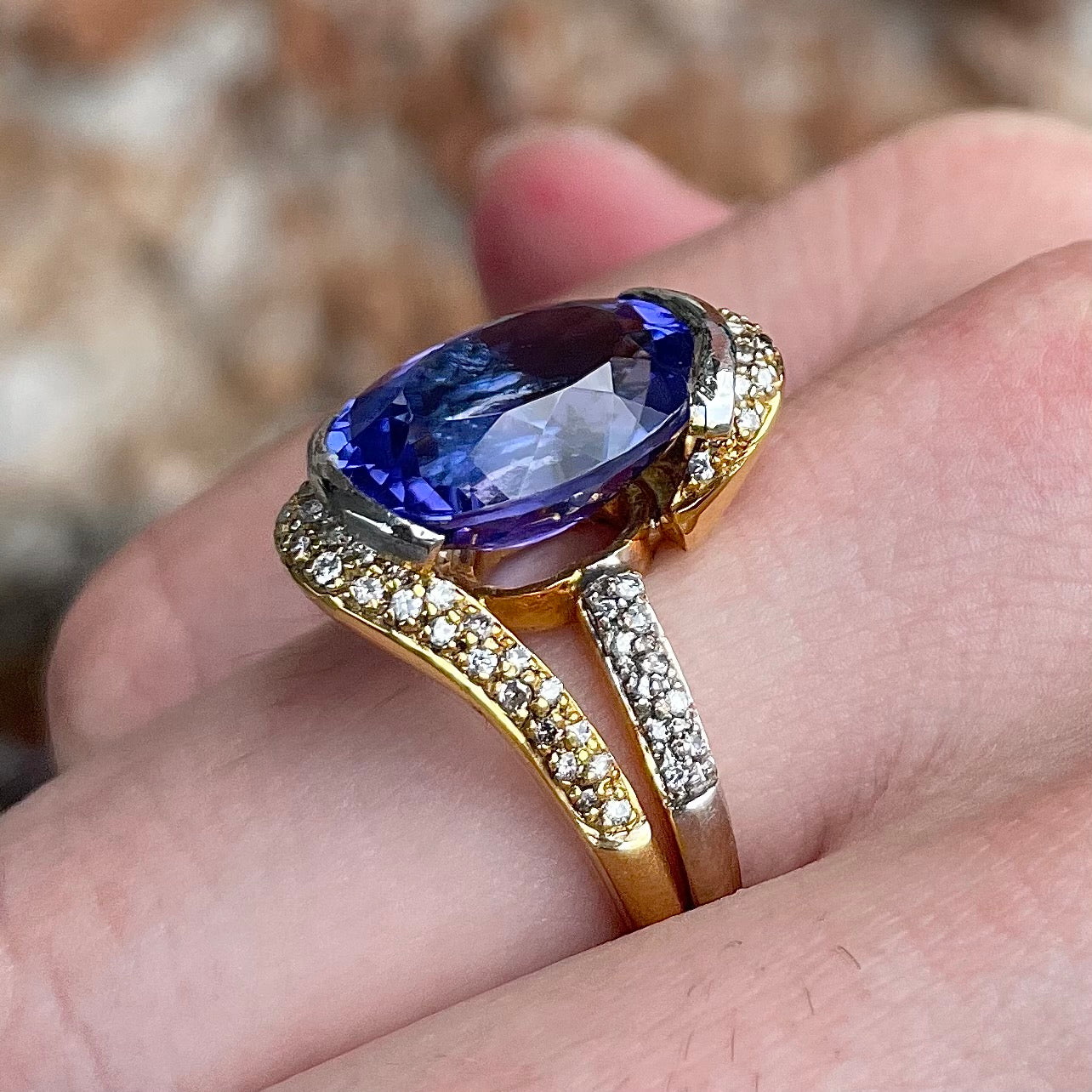A large, oval cut blue tanzanite set in a two tone yellow and white gold diamond ring.