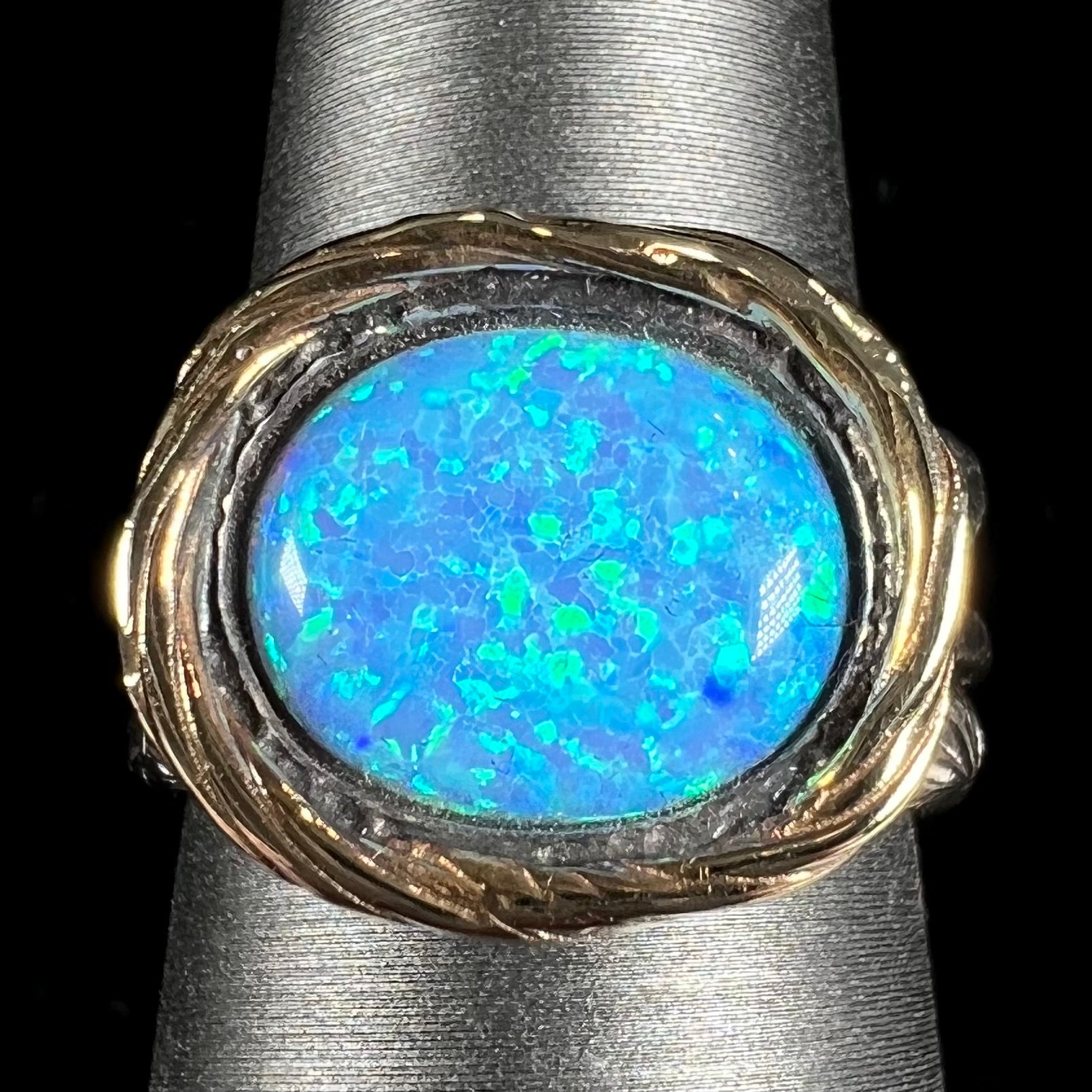 A filigree etched two tone silver and gold spinner ring set with a lab created black opal.