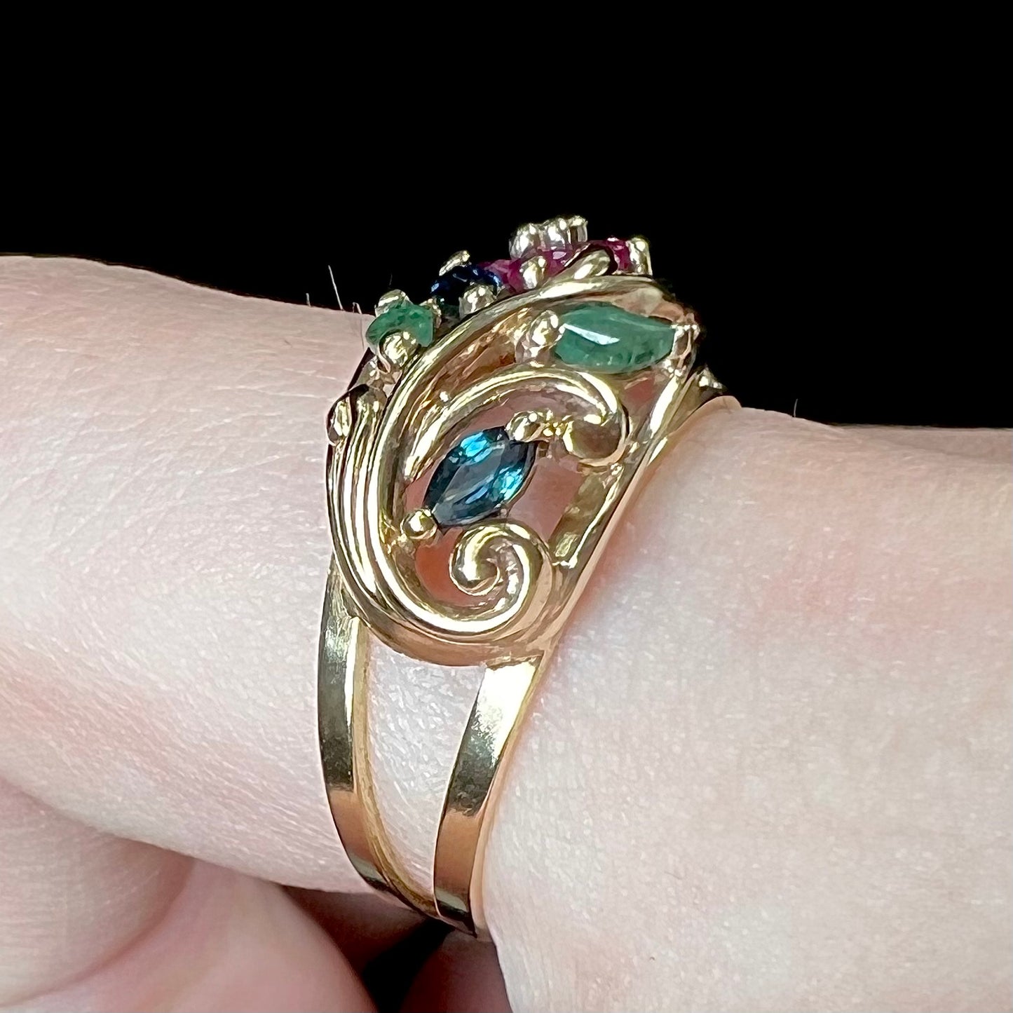 A yellow gold ladies' ring featuring the motif of a flower with leaves set with emeralds, rubies, sapphires, and a diamond.