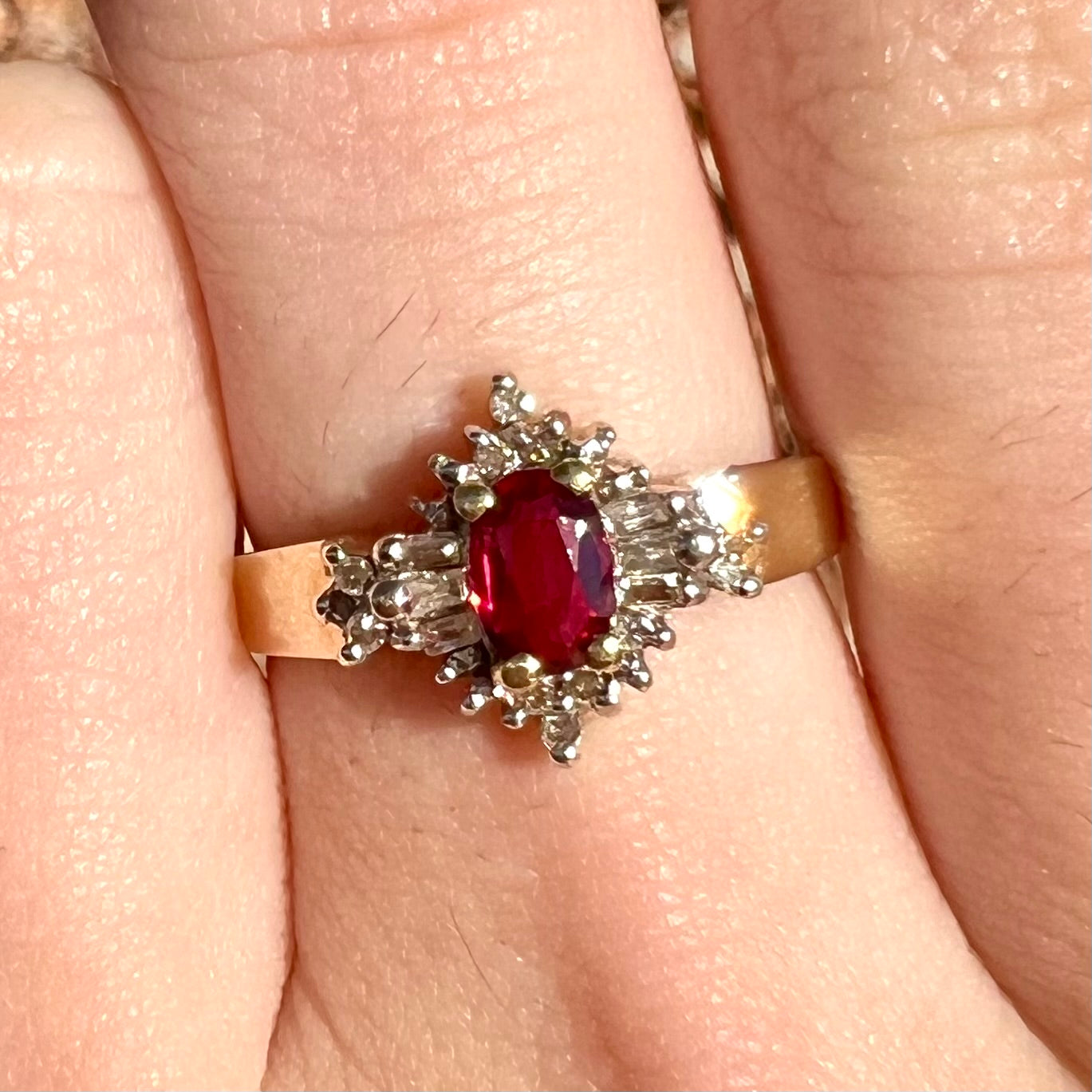 A yellow gold ring set with an oval cut red spinel and diamond rounds and baguettes.