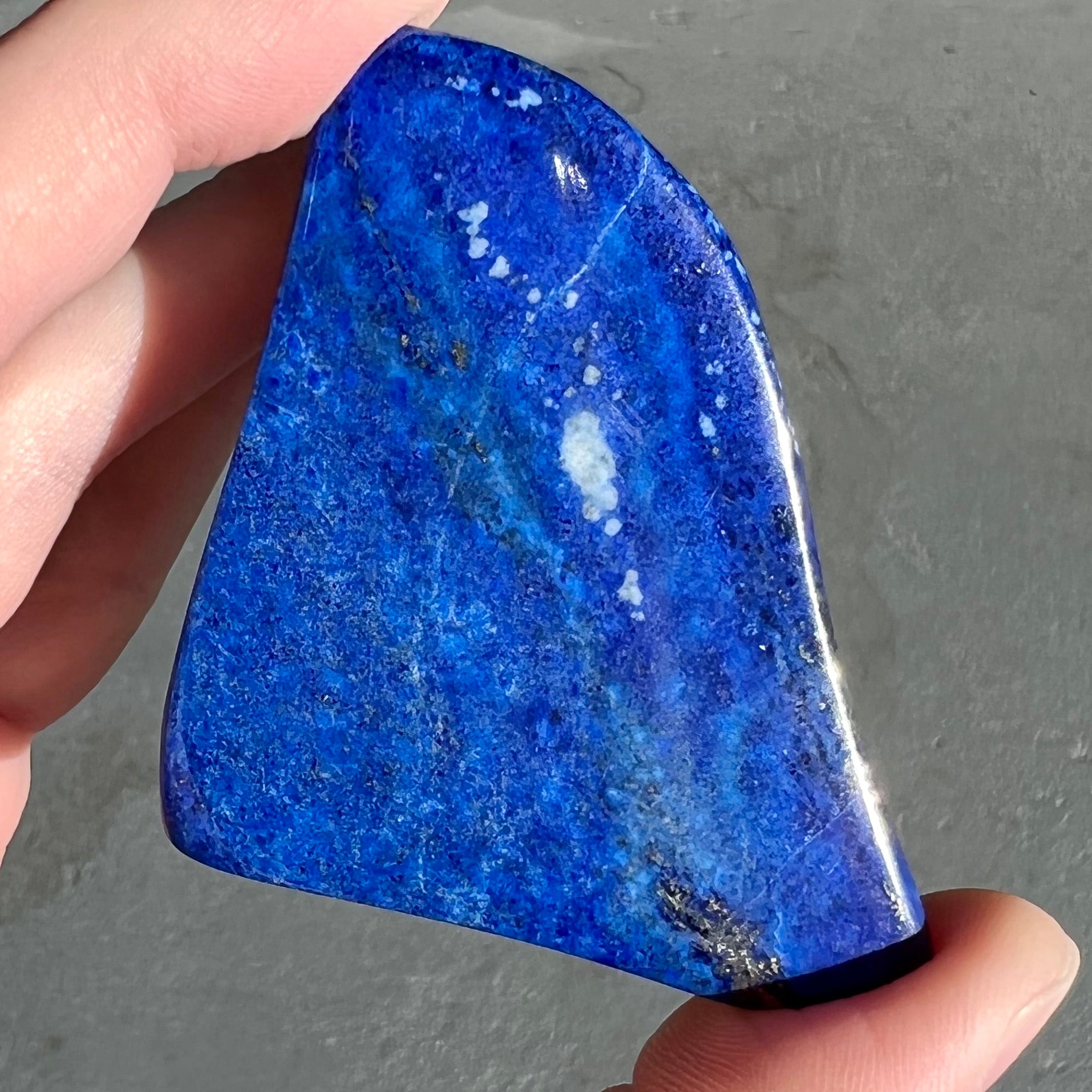 A loose polished sculpture made from royal blue lapis lazuli with golden pyrite inclusions.