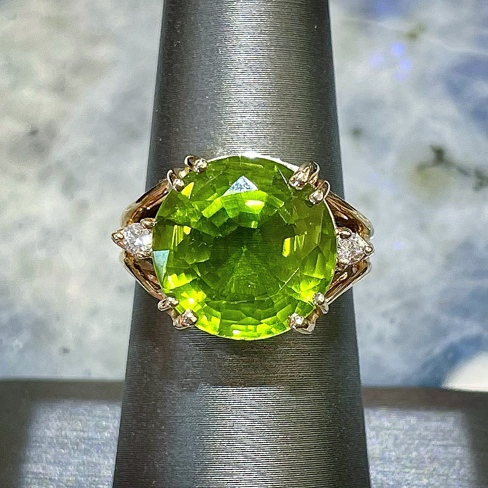 A ladies' round brilliant cut peridot statement ring set with two round diamond accents in yellow gold.