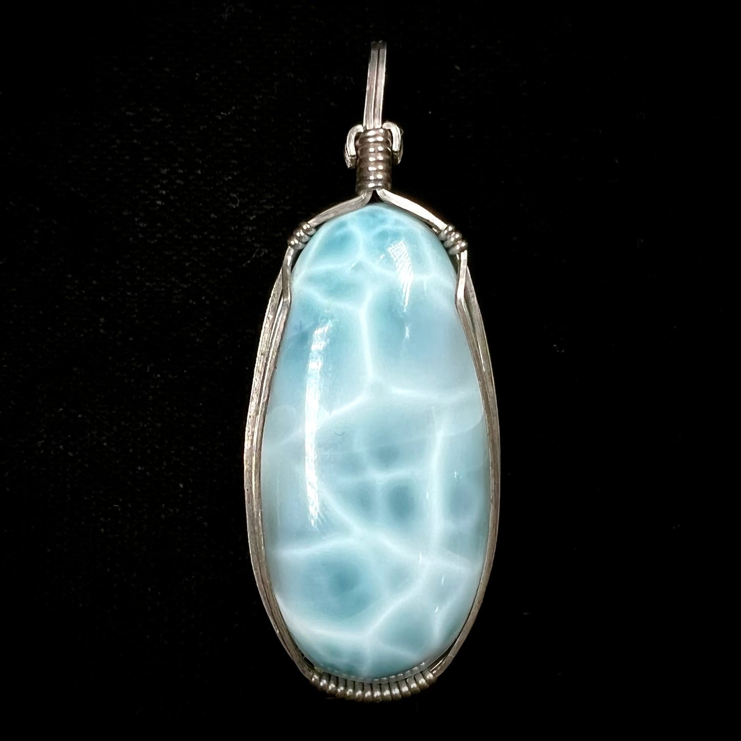 A large, oval cabochon cut blue larimar stone mounted in a sterling silver wire wrapped pendant.