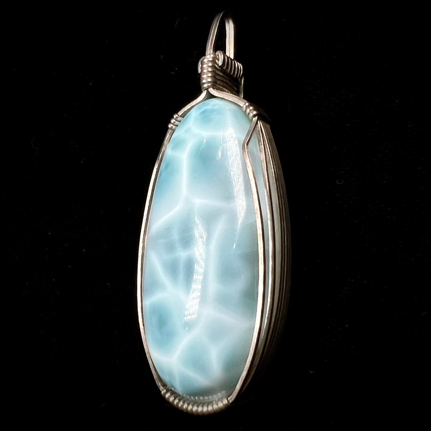 A large, oval cabochon cut blue larimar stone mounted in a sterling silver wire wrapped pendant.