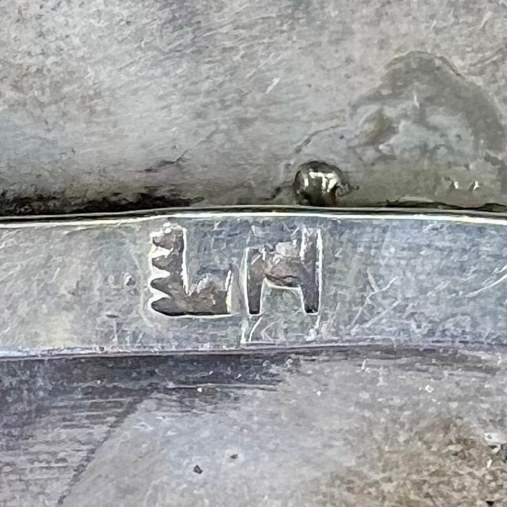 A sterling silver cuff bracelet featuring the motif of a stone inlaid hummingbird with petit point turquoise accents, handmade by Navajo artist Leo G. Harvey.