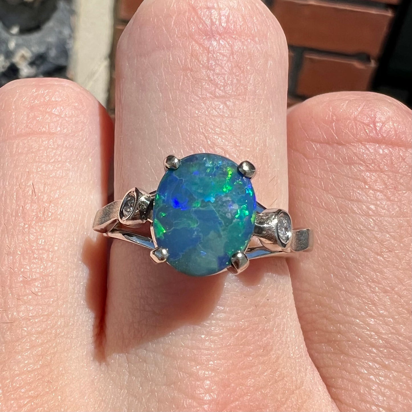 A white gold, oval cabochon cut black opal doublet ring set with two round diamond accent stones.