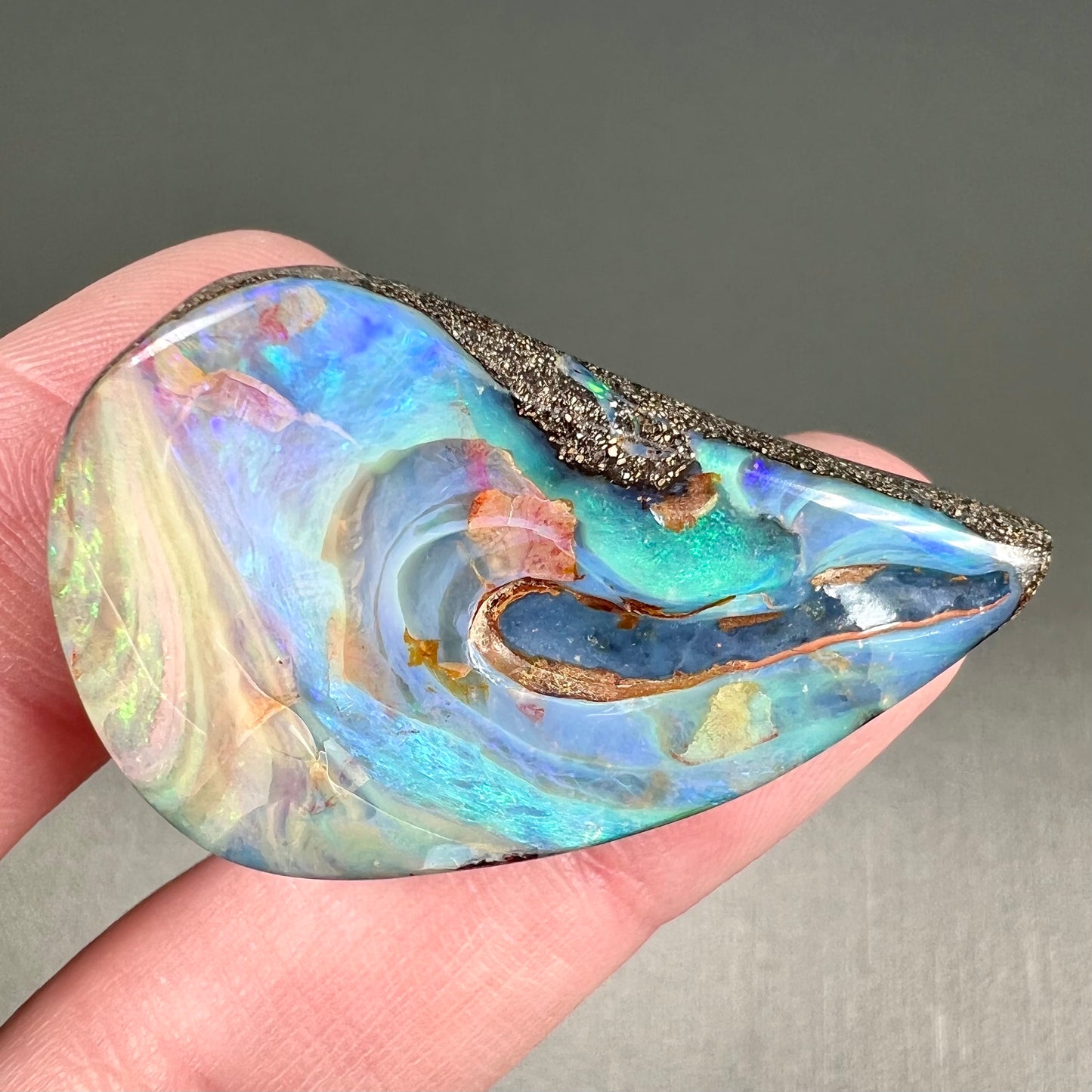 A polished pear shaped boulder opal stone from Quilpie, Australia. Predominant colors are blue, green, and aqua.