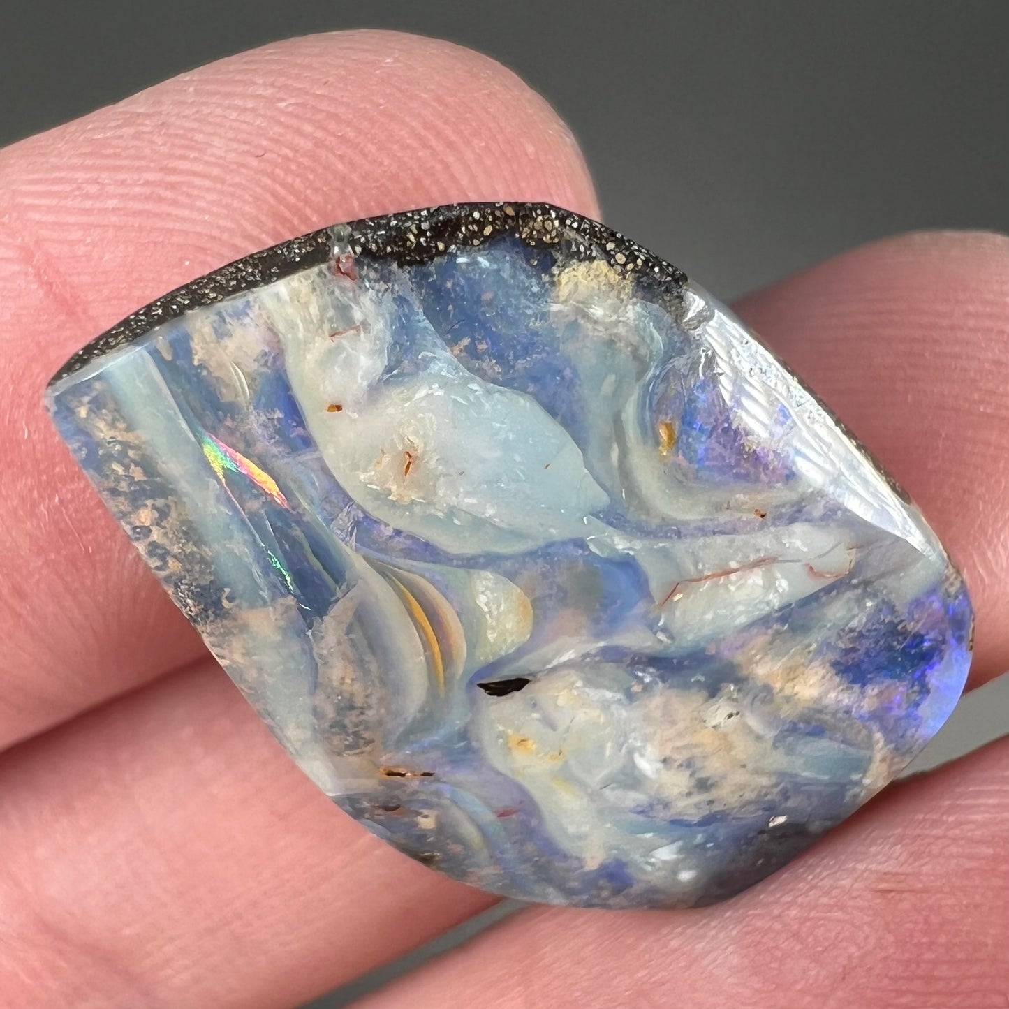 A loose, polished, freeform cut boulder opal stone from Queensland, Australia.