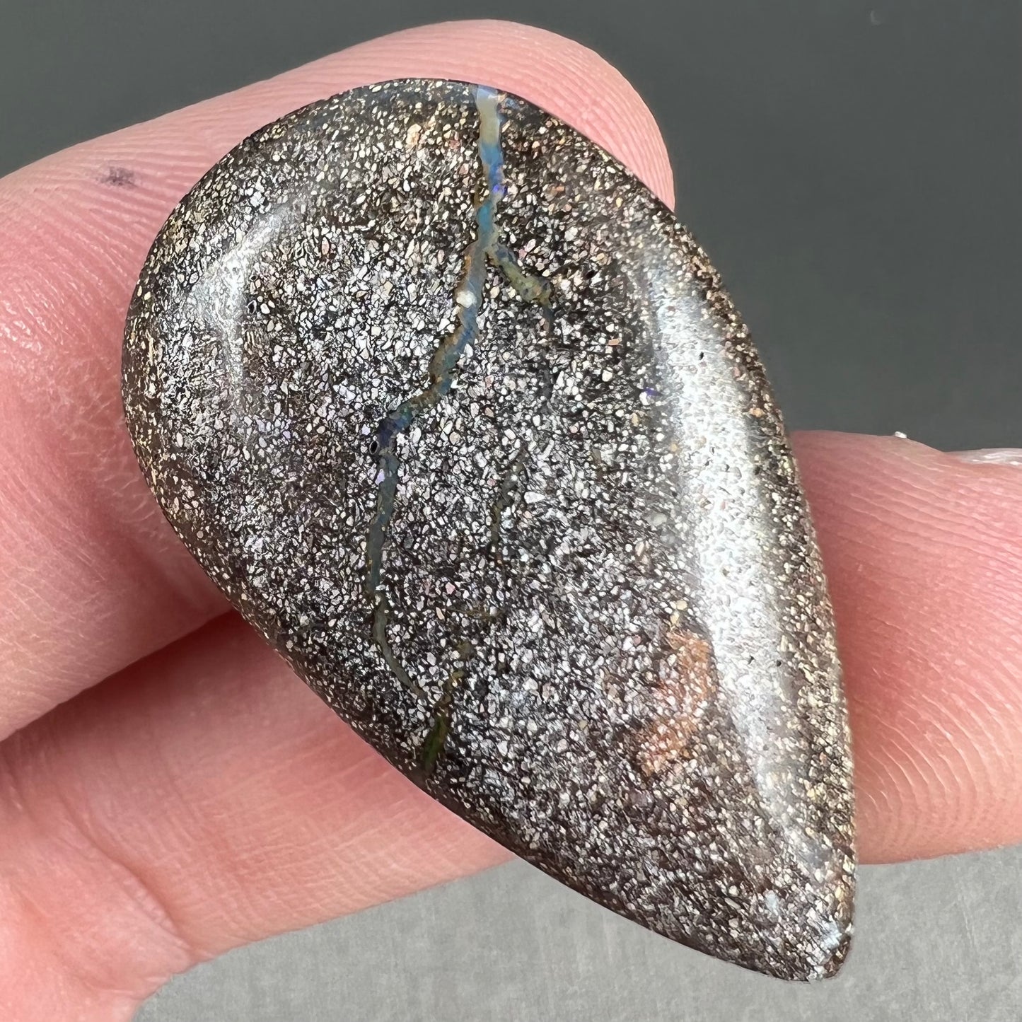 A loose, pear shaped boulder opal stone from Quilpie, Australia. The stone is predominantly blue, green, and purple with red and orange undertones.