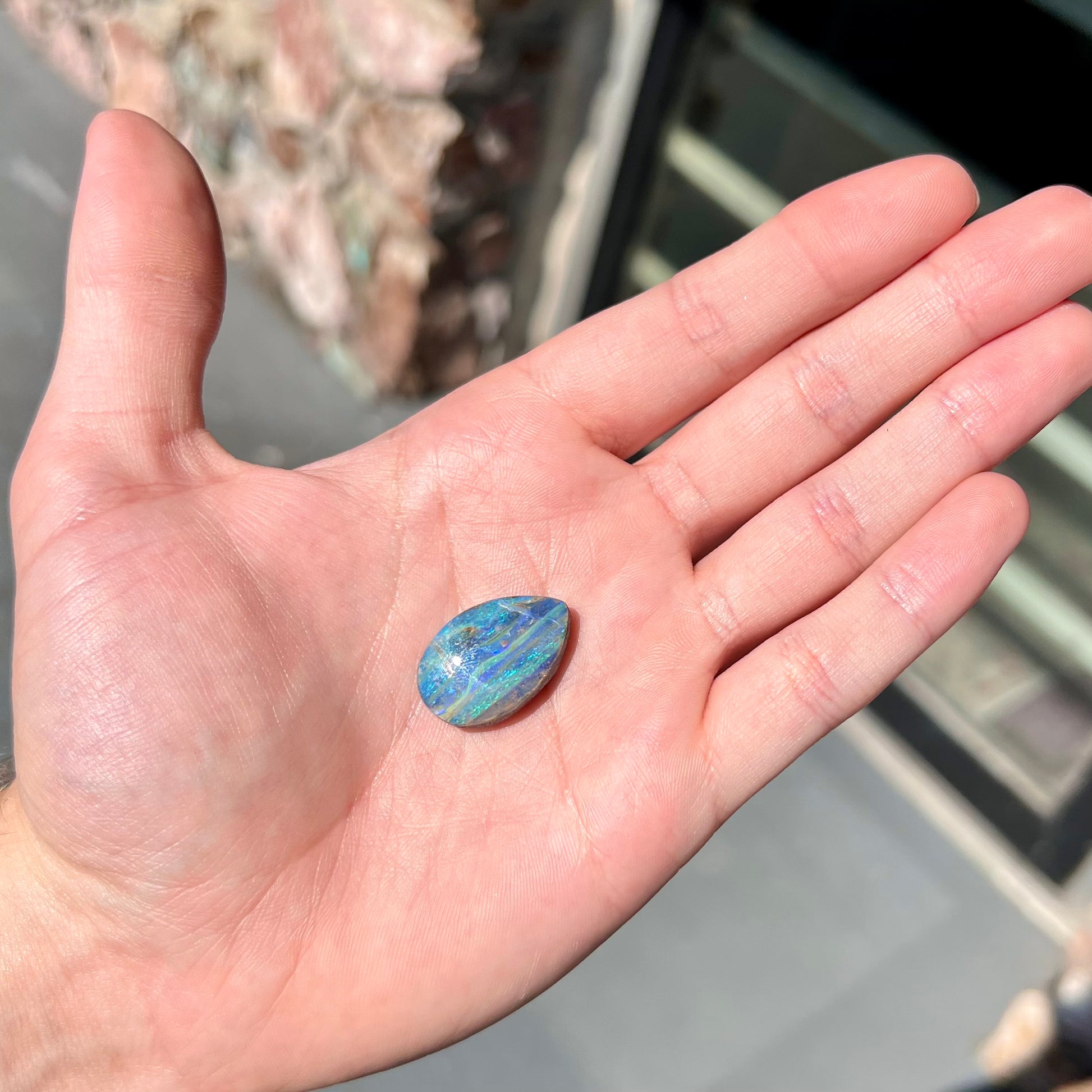 A loose, pear shaped Australian boulder opal stone.  The predominant colors are purple, green, and aqua.