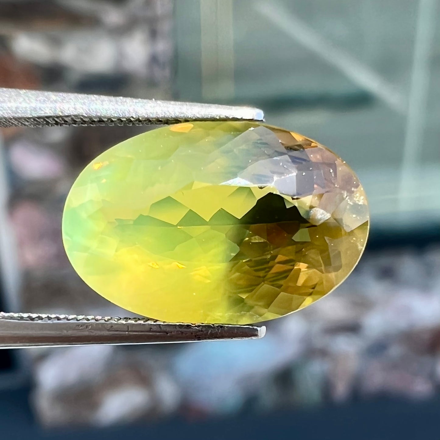 A loose, faceted oval cut bicolor chrysoberyl stone. The stone goes from neon green to dark green with orangey red flashes.