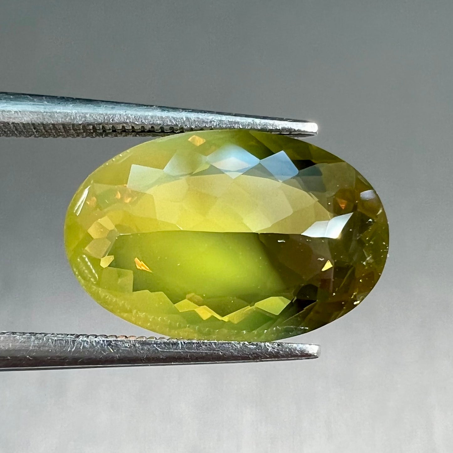 A loose, faceted oval cut bicolor chrysoberyl stone. The stone goes from neon green to dark green with orangey red flashes.